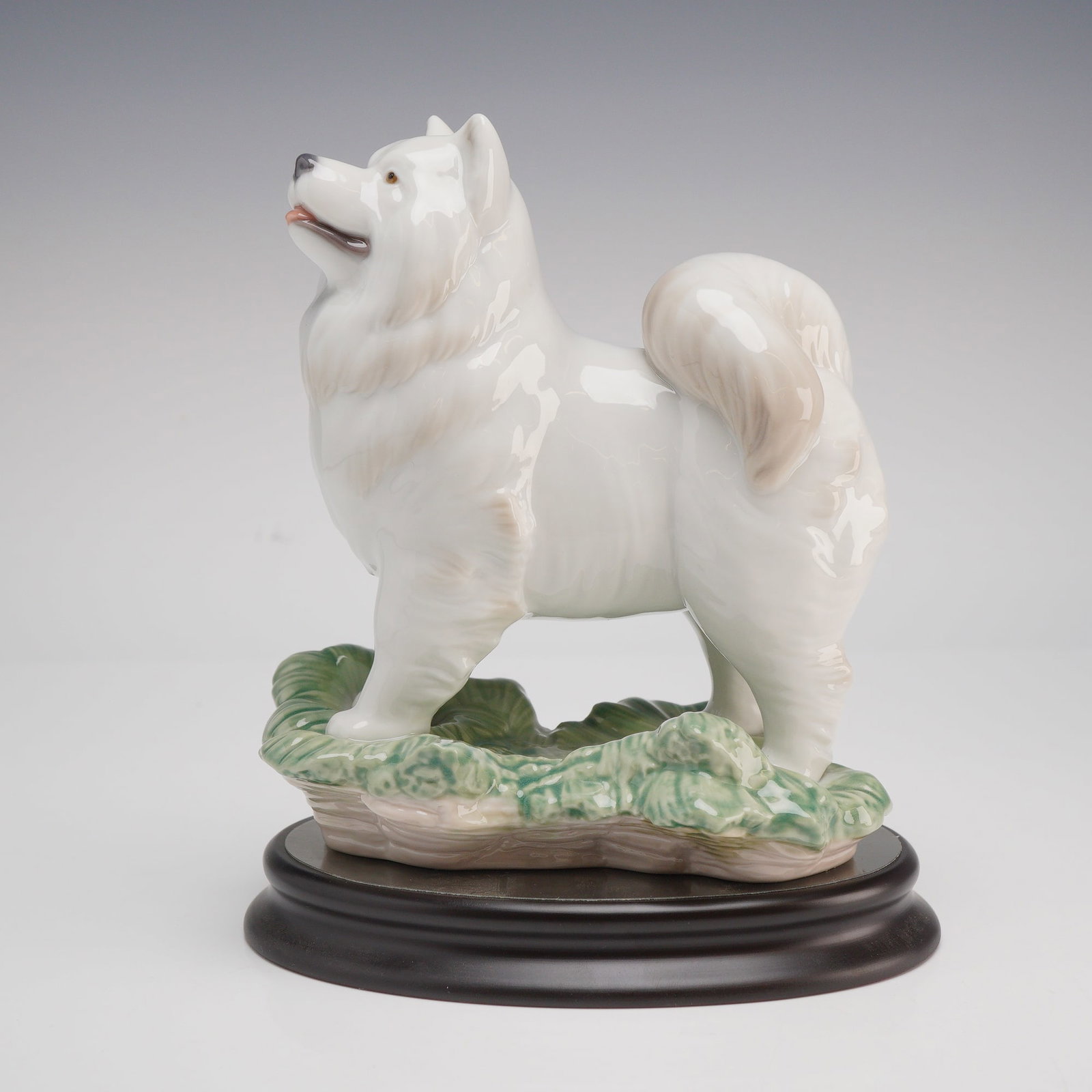 Lladro Porcelain Zodiac Collection Figurine The Dog 1008143: This high-gloss glazed porcelain figurine from the Lladro Zodiac Collection features a white dog with an alert expression and a curled, plumed tail, standing upon a green-glazed grassy base. The