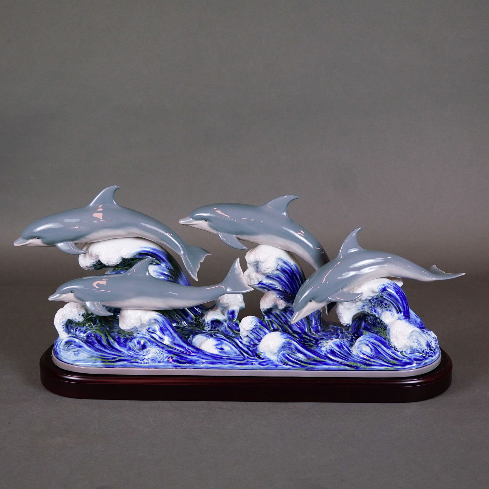 Lladro Dolphins' Dance Porcelain Sculpture Model 6436: Lladro glossy sculpture model 6436, titled Dolphins' Dance. This porcelain figurine depicts a group of dolphins leaping through crashing waves. The dolphins are rendered in a pale greenish-blue glaze