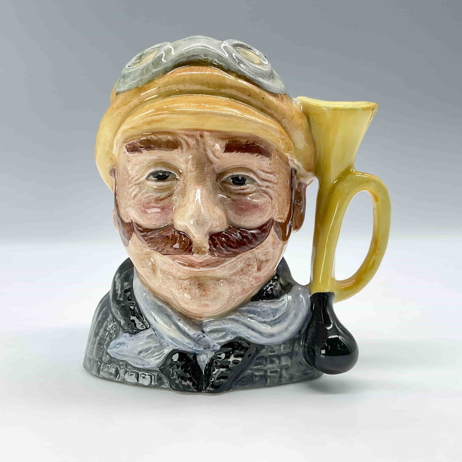 Veteran Motorist D6637 - Small - Royal Doulton Character Jug: Fine bone China jug depicting English gentleman in yellow hat; black collar; grey coat and scarf. Royal Doulton backstamp. ArtistDavid B. Biggs Dimensions4.25 "L x 3" W x 4" H Date or Era1972