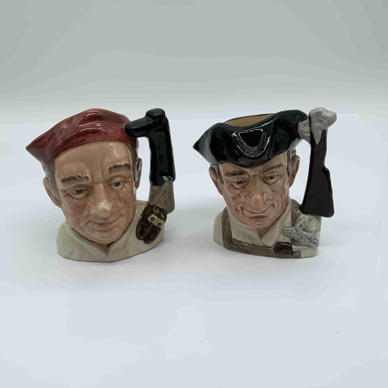 2pc Royal Doulton Sm Character Jugs, Boot Maker & Gunsmith: This lot features two Royal Doulton Character Jugs from the celebrated 'Character Jugs from Williamsburg' series. The first is the Boot Maker (D6579, c.1962), which beautifully captures the portrait
