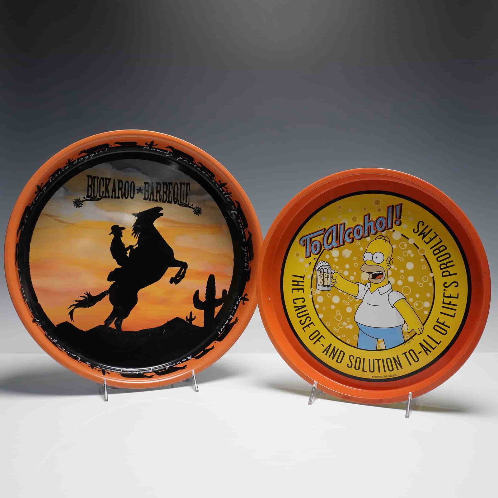 2pc Decorative Metal Trays, Homer Simpson and Buckaroo Barbeque: Two vintage decorative round metal trays, each with an orange rim. The first tray features a colorful depiction of Homer Simpson raising a beer with the phrase "To Alcohol! The cause of and solution