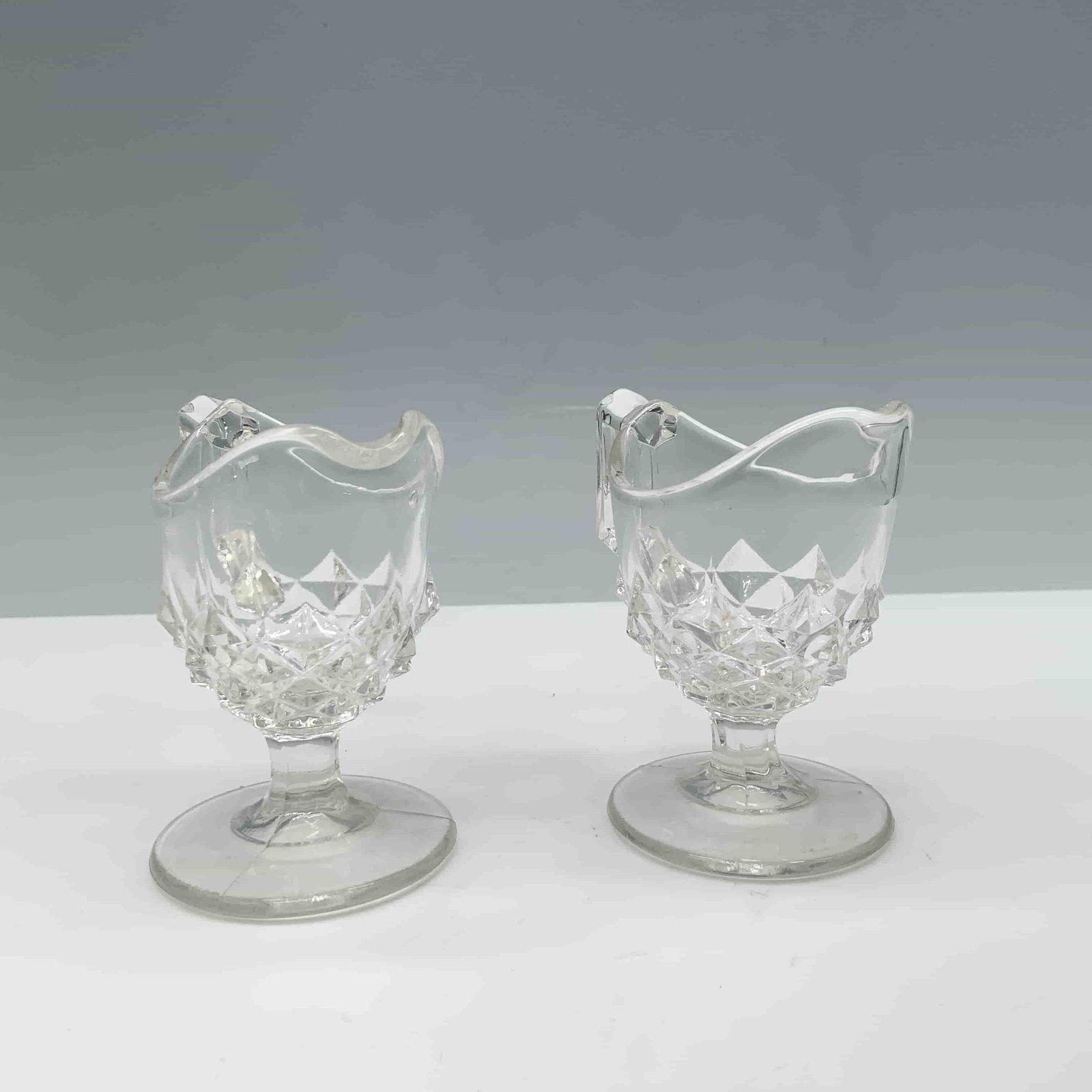 Pair of Art Glass Children's Creamer Jugs: Adorable duo of sawtooth variation clear glass jugs with handles and footing. Dimensions3.25"L x 2"W x 3"H Date or Era20th century