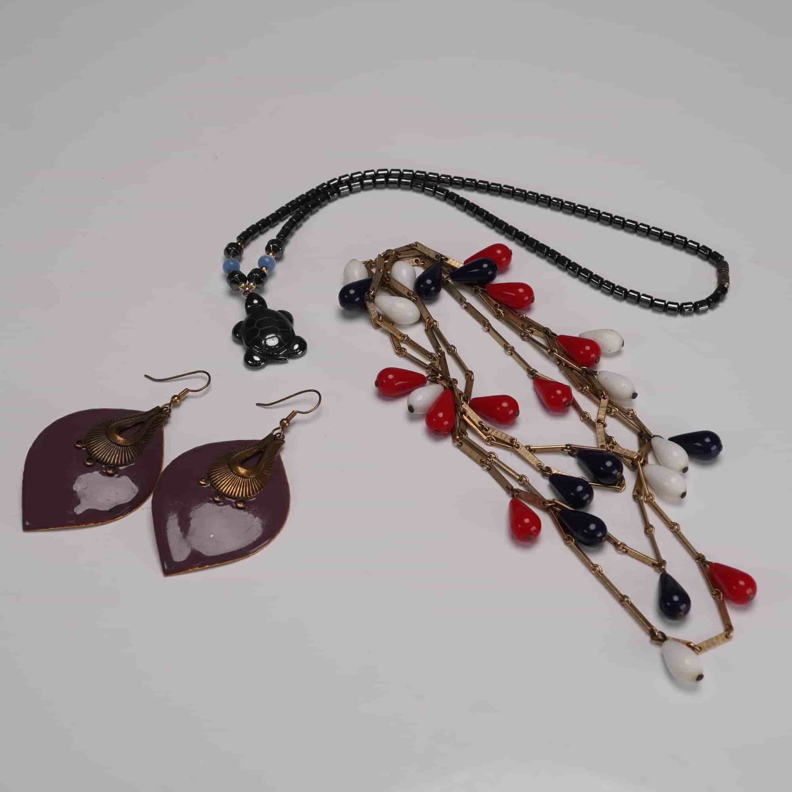 4pc Beaded Jewelry Group, Enameled Earrings, Turtle Pendant & Necklace: Group of four assorted costume jewelry pieces, including a black beaded necklace featuring a carved hematite-style turtle pendant with blue and gold-tone accent beads and a twist-barrel clasp; a