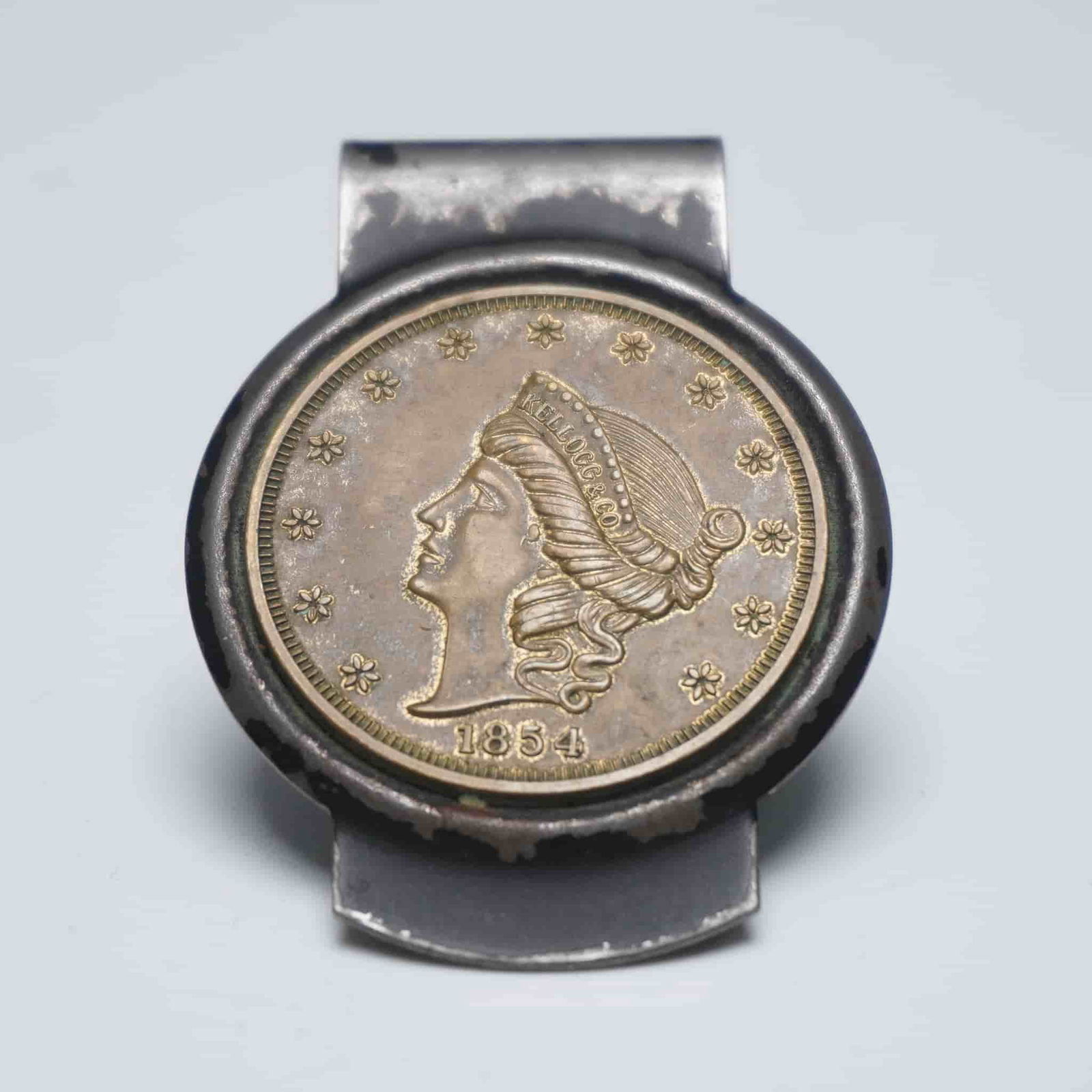 Kellogg & Co. 1854 Liberty Head Replica Coin Money Clip: A vintage-style metal money clip featuring an embedded replica coin depicting the 1854 Liberty Head design. The obverse side of the replica displays a left-facing profile of Lady Liberty surrounded