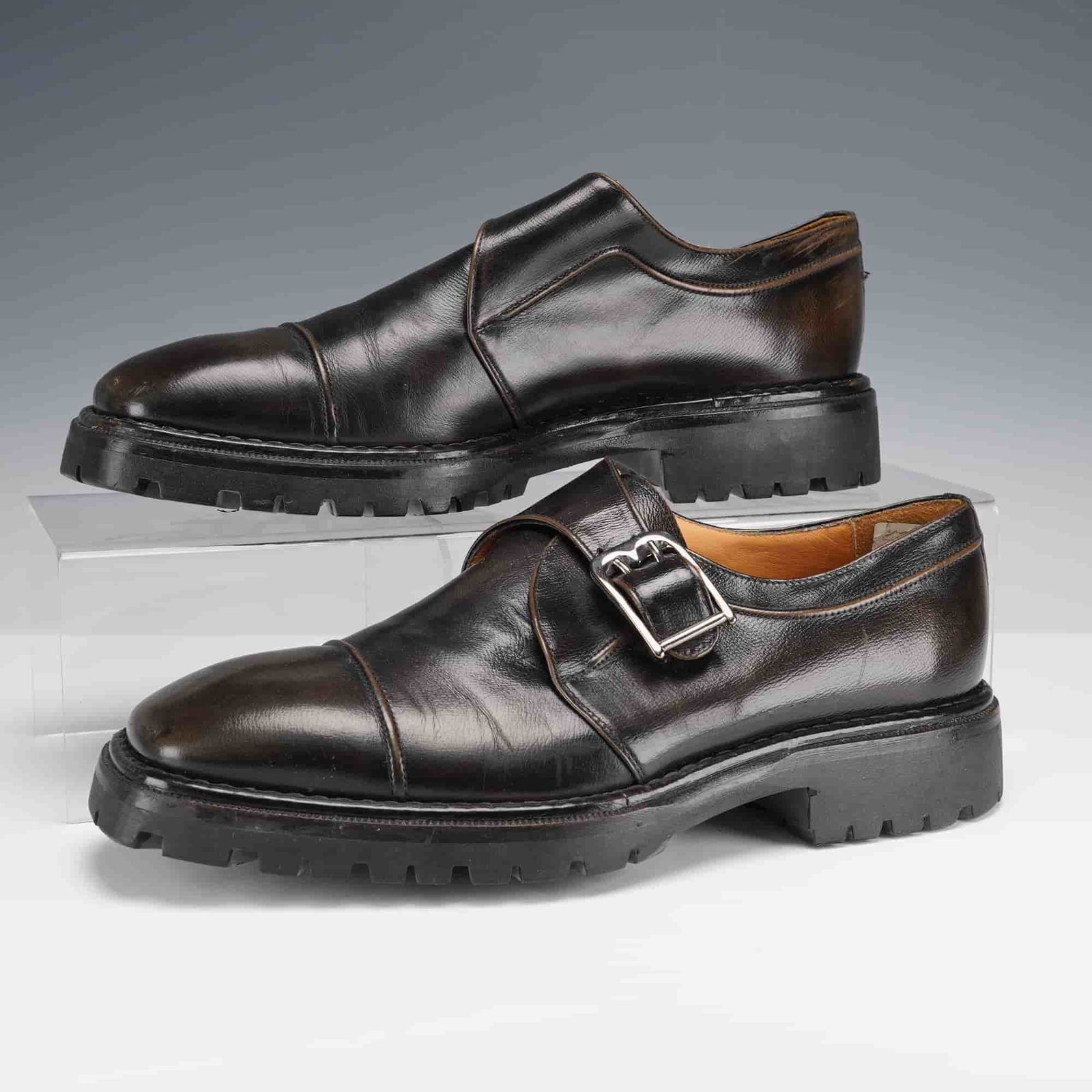 Bally Men's Monk Strap Shoes, Black Leather: A pair of Bally black leather monk strap shoes featuring a single buckle closure and cap toe design. The shoes have rugged rubber lug soles stamped Bally and fully leather-lined interiors in tan. 