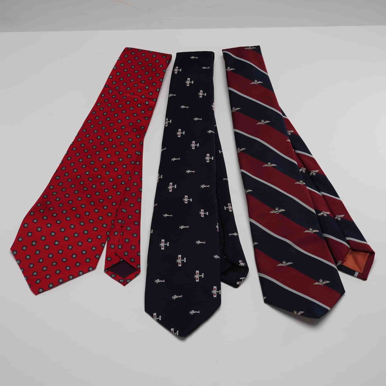 3pc Necktie Collection, Bert Pulitzer, RAF, Charing Cross: Set of three neckties including a red Bert Pulitzer tie with a small repeating geometric pattern, a burgundy and navy striped tie marked polyester and made in England featuring RAF winged emblem