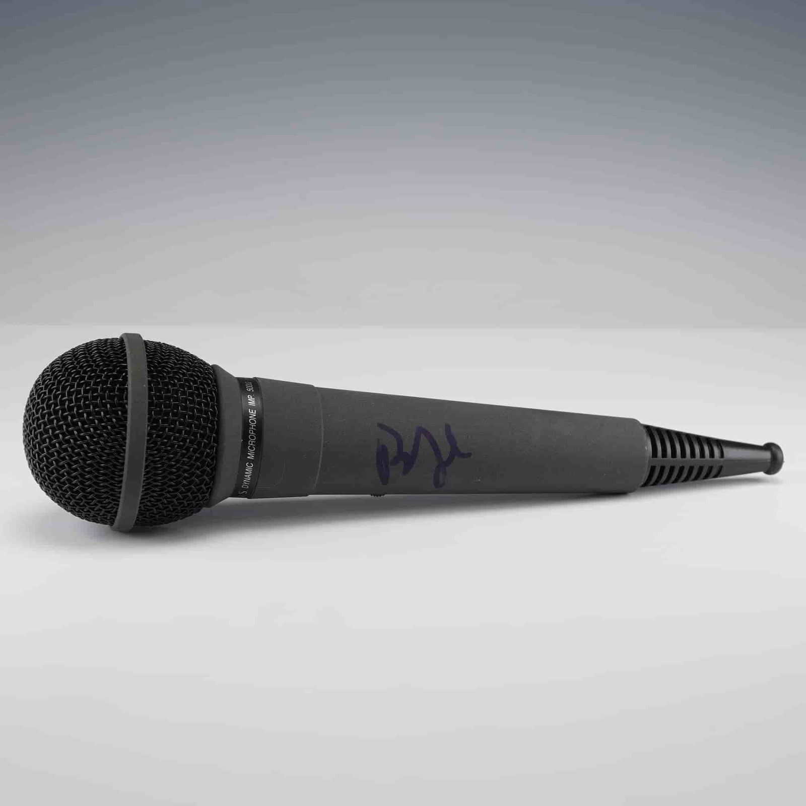 Autographed Gray Dynamic Microphone: Gray dynamic microphone with black grille and on/off switch, featuring a bold autograph in dark blue marker along the handle. The signature is stylized and not fully legible. Autograph positioned on
