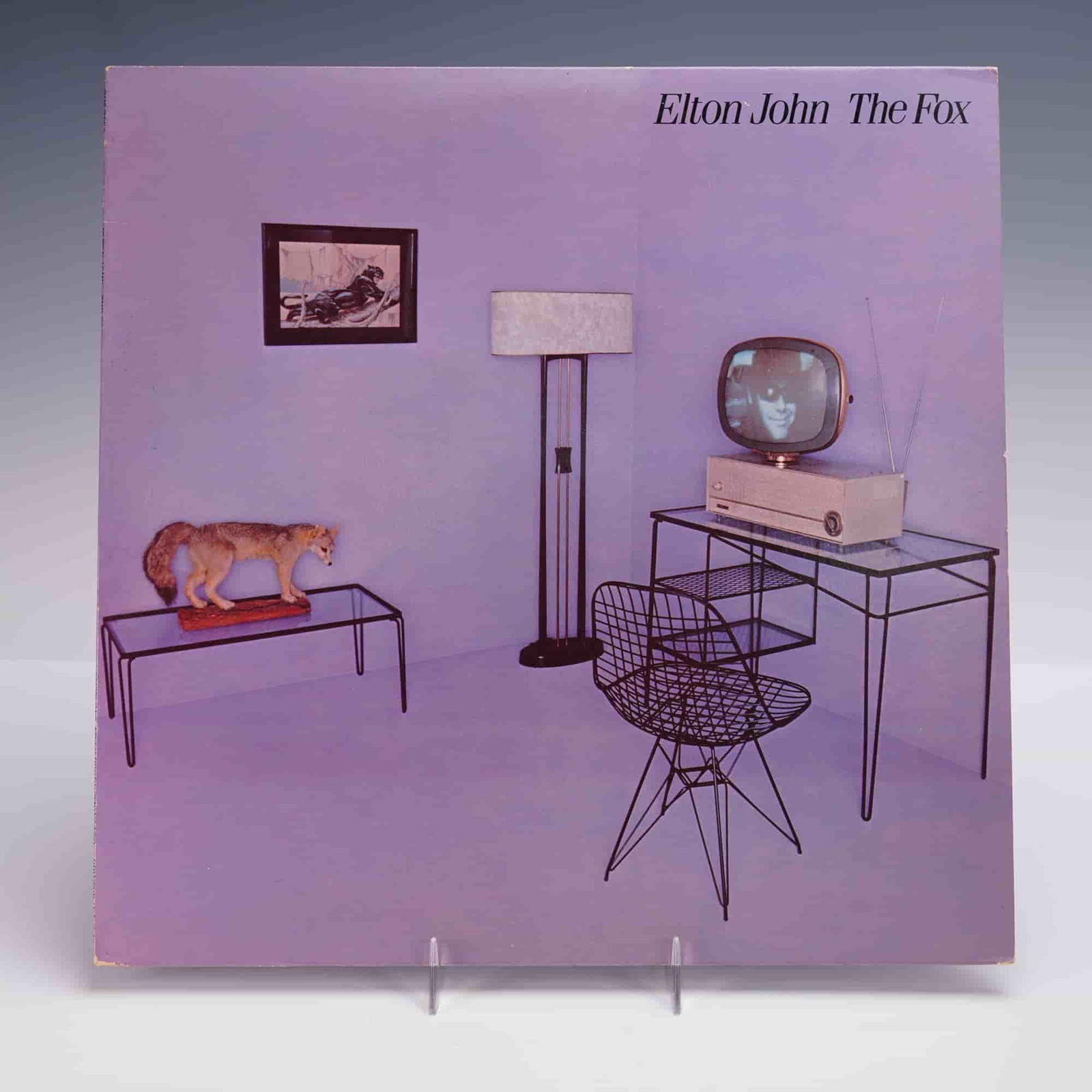 Geffen Records Elton John Vinyl Record, The Fox: A 1981 U.S. pressing of Elton John's "The Fox" LP vinyl album, released by Geffen Records. The album cover features a minimalistic and surreal interior room scene rendered in violet tones, with modern