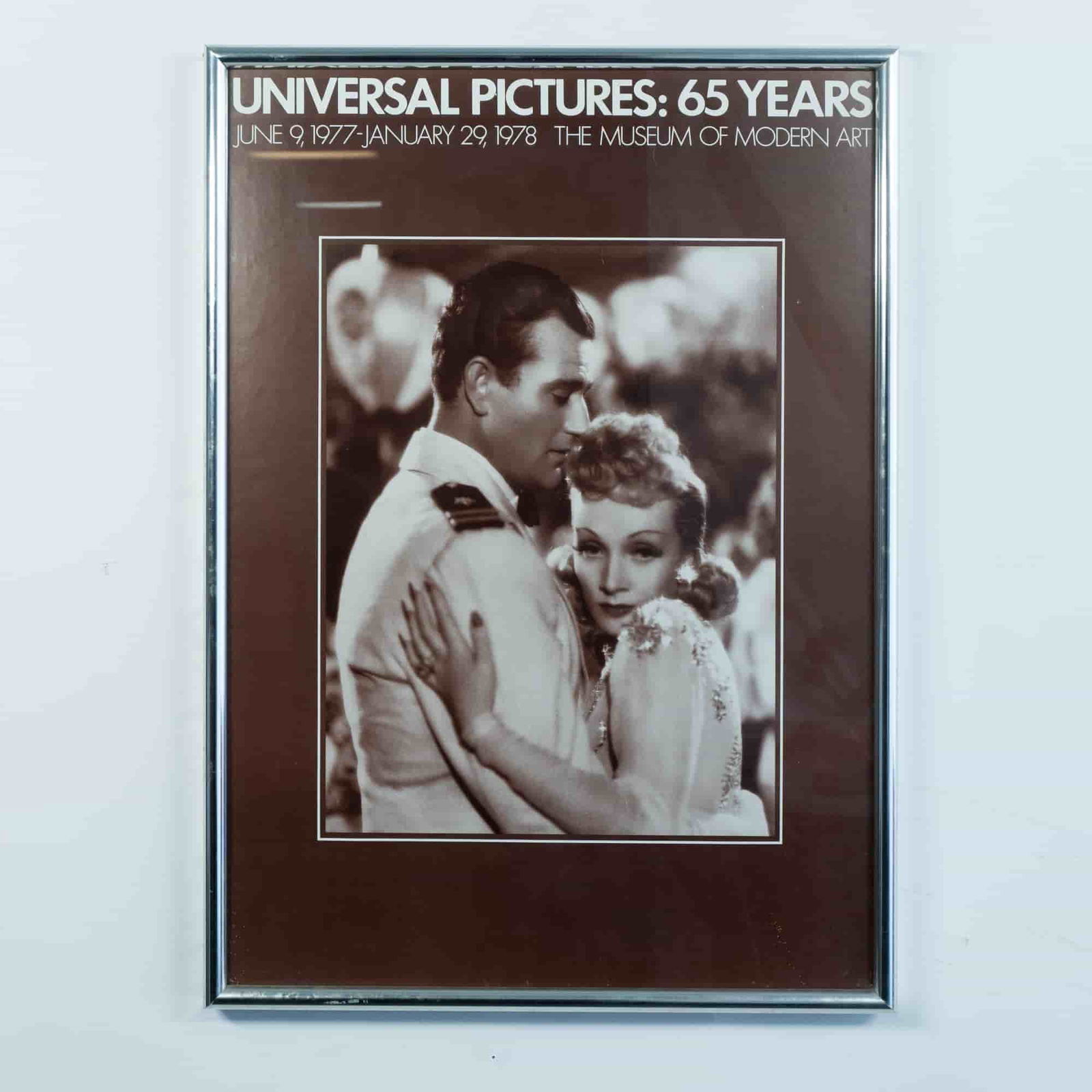 Original MoMA Universal Pictures: 65 Years Exhibition Poster: Original Museum of Modern Art Universal Pictures: 65 Years exhibition poster featuring Marlene Dietrich and John Wayne in a still from the 1940s movie Seven Sinners. Sight size: 16.50"L x 23.50"H. Fra