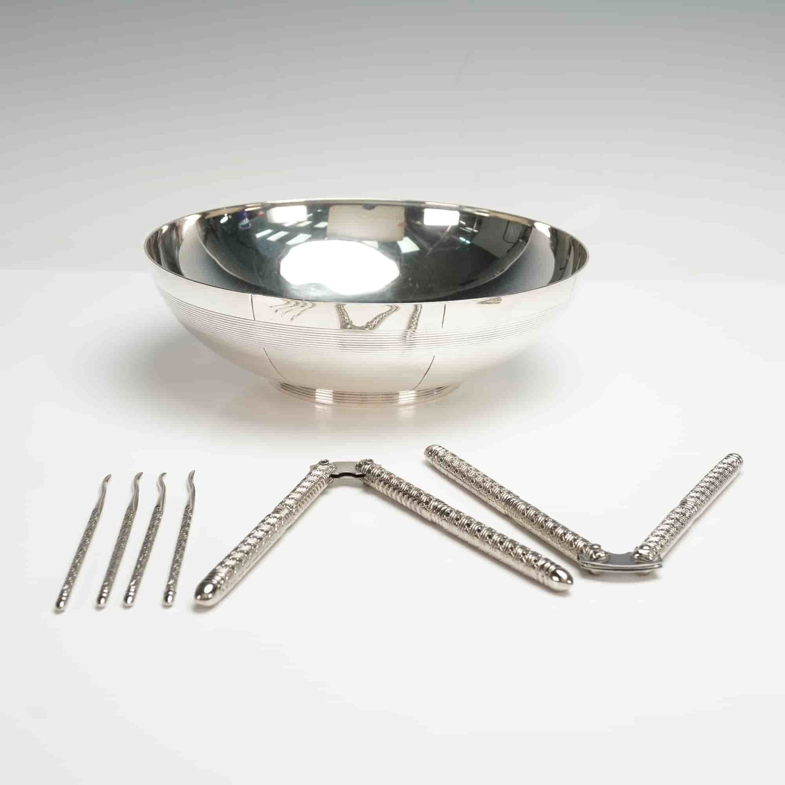 7pc Vera Wang Serving Bowl with Seafood Utensils: This Vera Wang silver-tone set includes a round serving bowl and six seafood utensils. The bowl has a reflective finish with fine horizontal line detailing and is marked Vera Wang on the underside.