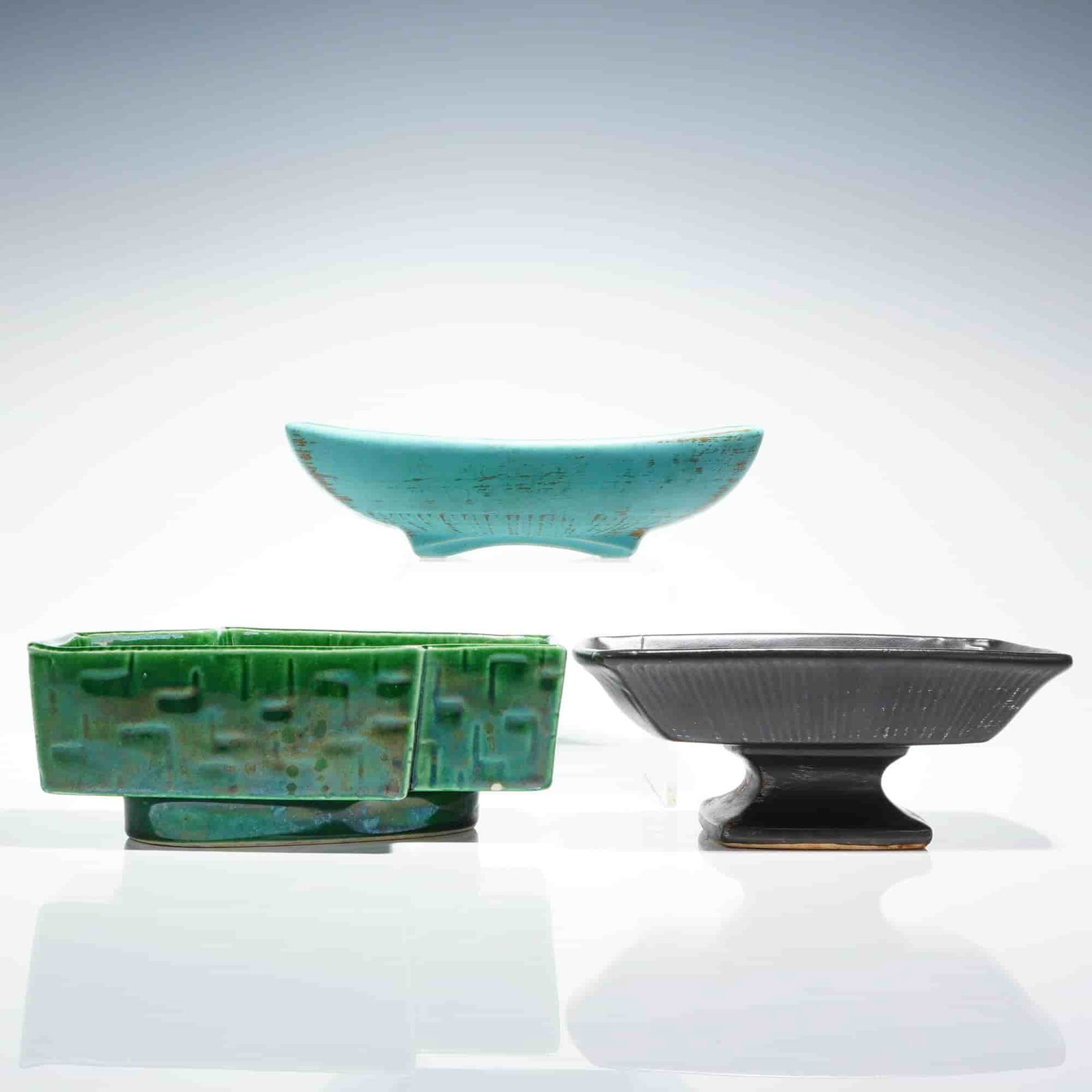 A Trio of Mid-Century Modern McCoy Pottery Planters and Dishes: A collection of three (3pc) vintage McCoy Pottery planters and dishes executed in glazed earthenware, reflecting a Mid-Century Modern aesthetic. The collection includes a boat-shaped vessel finished i