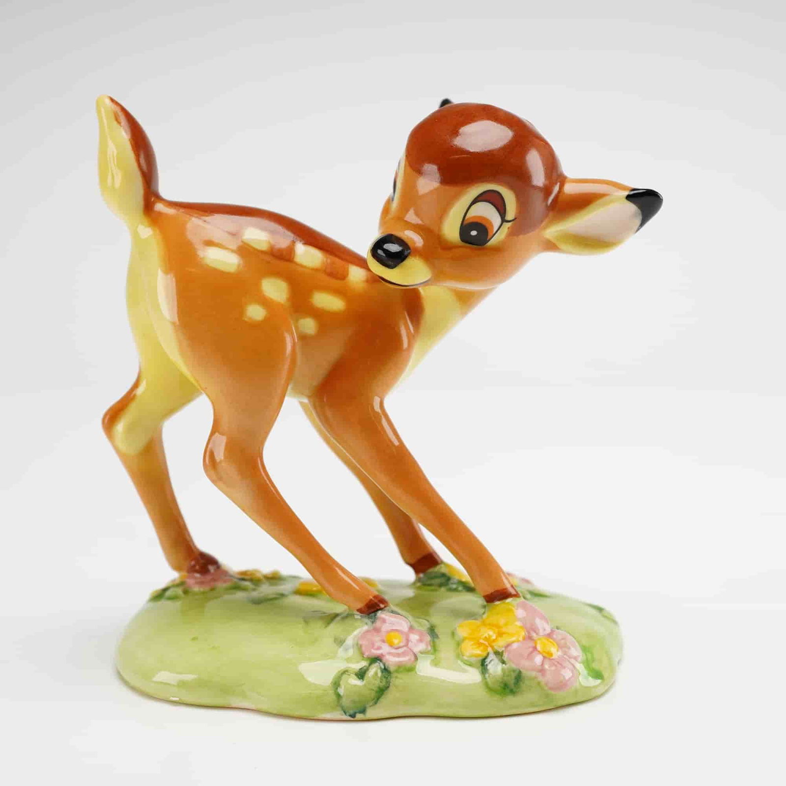 Royal Doulton Disney Figurine, Bambi FC1: This hand-decorated porcelain figurine depicts the character Bambi standing on a grassy base accented with pink and yellow flowers, finished with a high-gloss glaze. The underside bears the Royal Doul