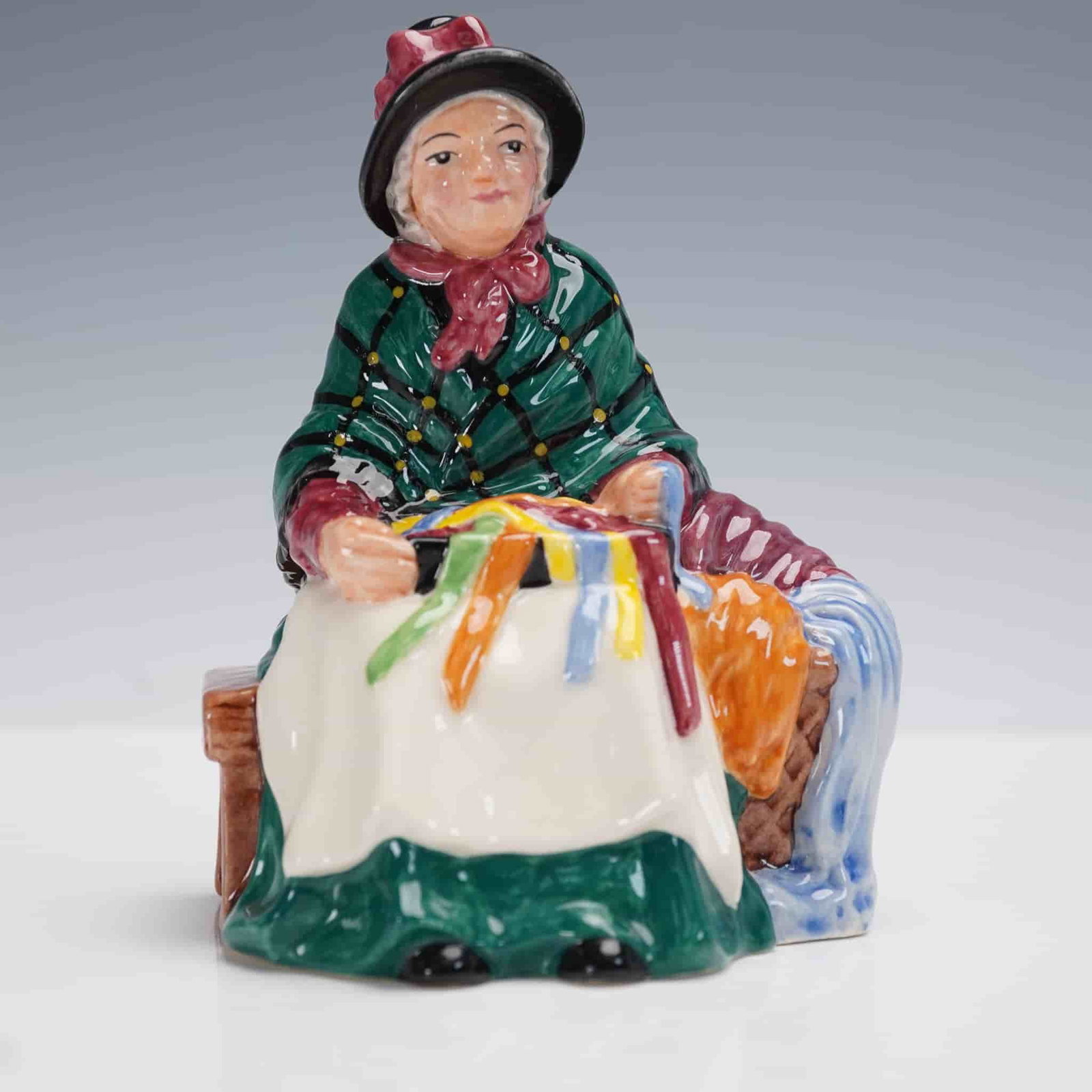Royal Doulton Figurine, Silks & Ribbons HN4808: Issued in 2003 as part of the Miniature Street Vendors collection, this Royal Doulton figurine titled Silks & Ribbons (HN4808) captures a charming vendor arranging colorful textiles with intricate det