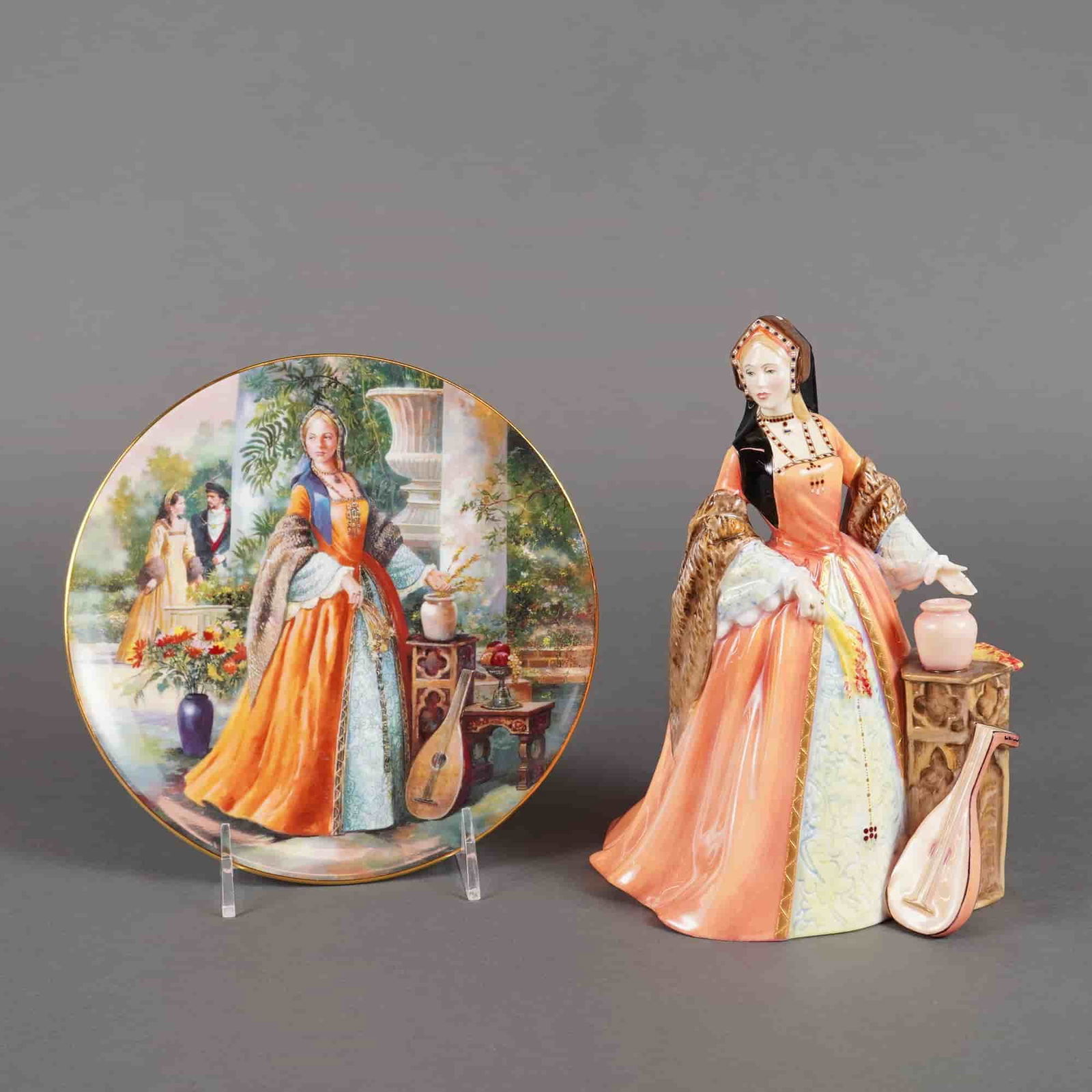 2pc Royal Doulton and Royal Kent Figurine and Plate, Jane Seymour: The glazed Royal Doulton porcelain figurine is modeled in Tudor dress, predominantly colored in orange and blue-green tones, standing next to an ornately carved table supporting a lute and a small vas