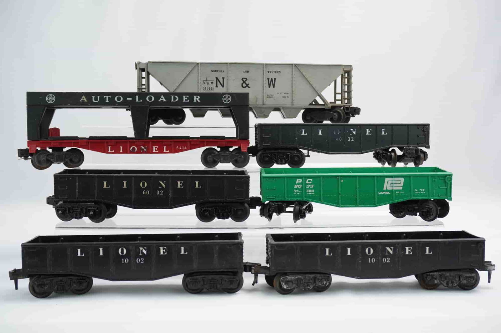 7pc Lionel O Gauge Model Train Rolling Stock Cars: A collection of seven vintage Lionel O Gauge rolling stock cars, constructed primarily from molded plastic and metal components. The assemblage includes a light gray NORFOLK AND WESTERN N&W hopper car