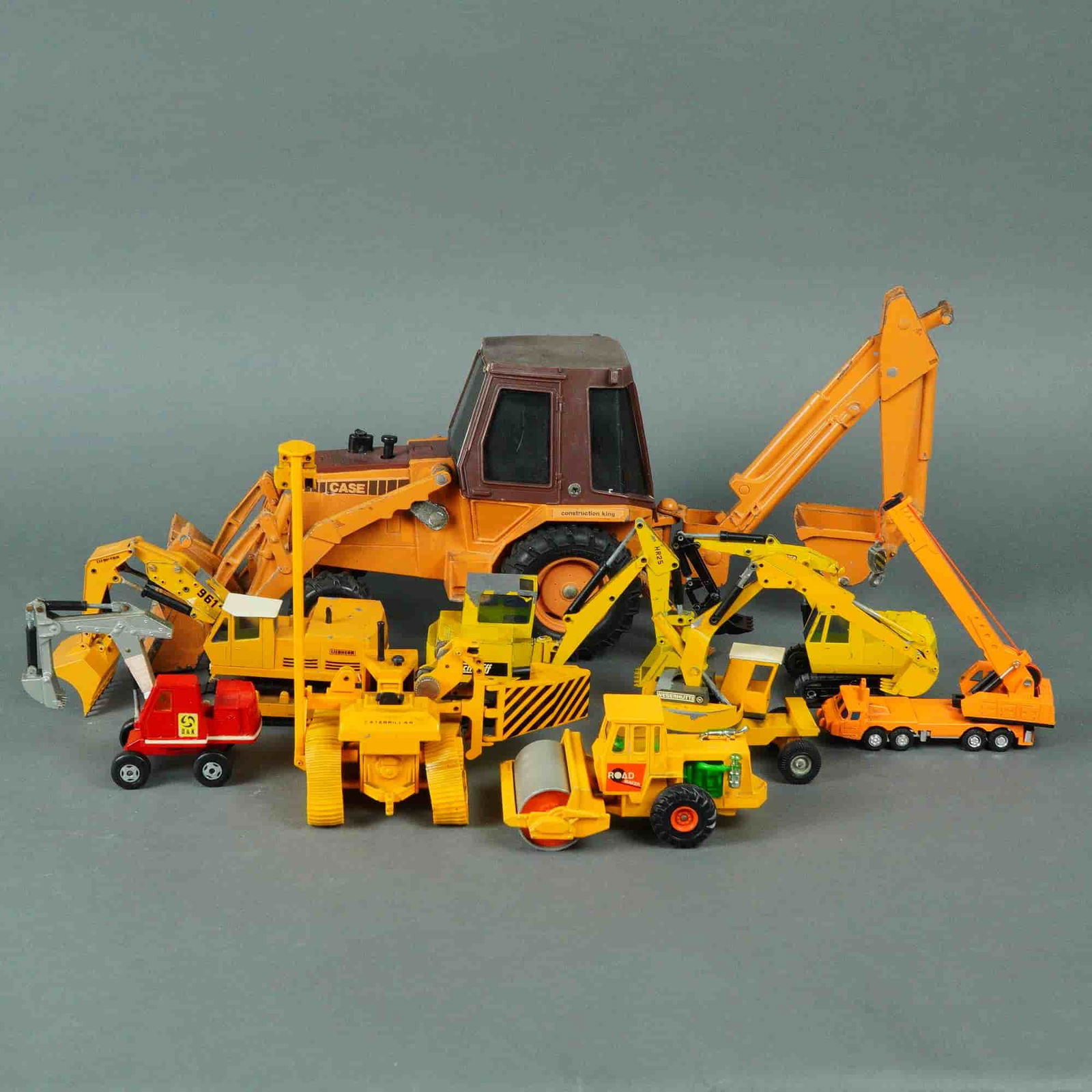 10 Vintage Die Cast Construction Vehicles incl Ertl Case 580E: A collection of ten vintage die-cast metal and plastic construction vehicle models, primarily finished in construction yellow and orange. The collection consists of nine distinct vehicles and one