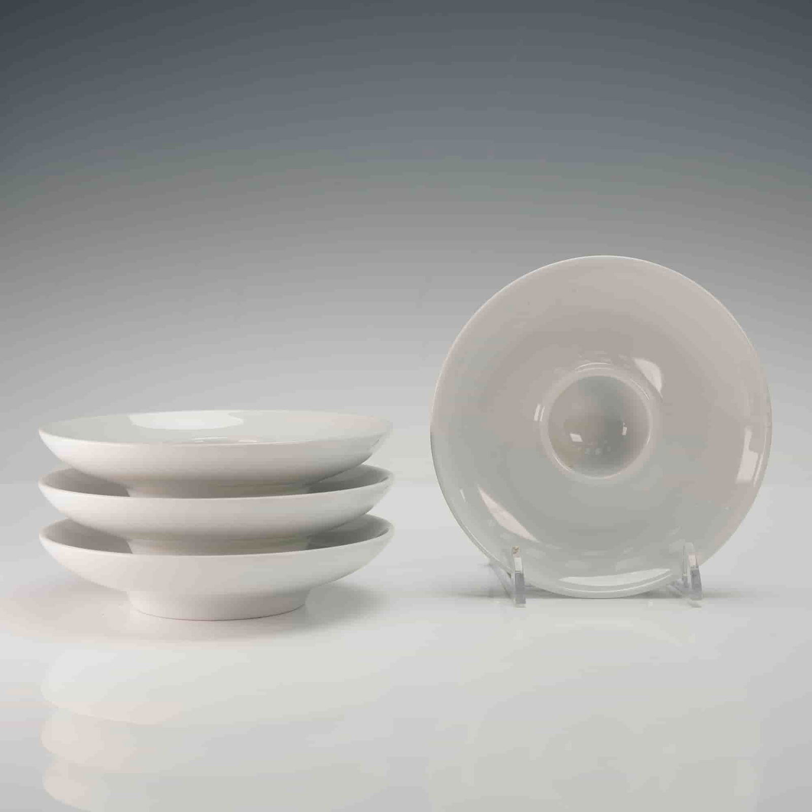4pc Thomas Rosenthal White Porcelain Candle Holders: Each formed as a shallow circular dish with a raised central well designed to securely accommodate a taper candle, displaying smooth, clean lines and a uniform white glaze; the underside of each piece