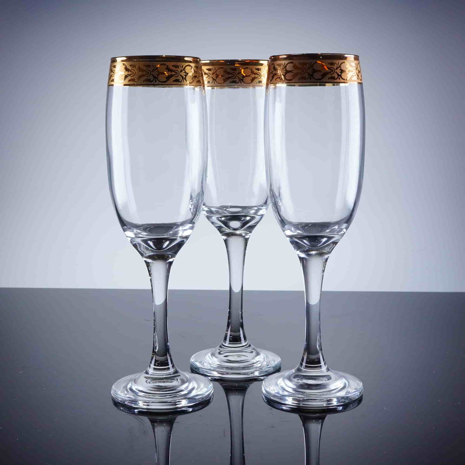 3pc Gold Rim Champagne Flutes: A trio of champagne flutes constructed of clear glass and featuring a tall, narrow bowl, slender stem, and circular foot. The defining characteristic is the wide, continuous band of intricate gold dec