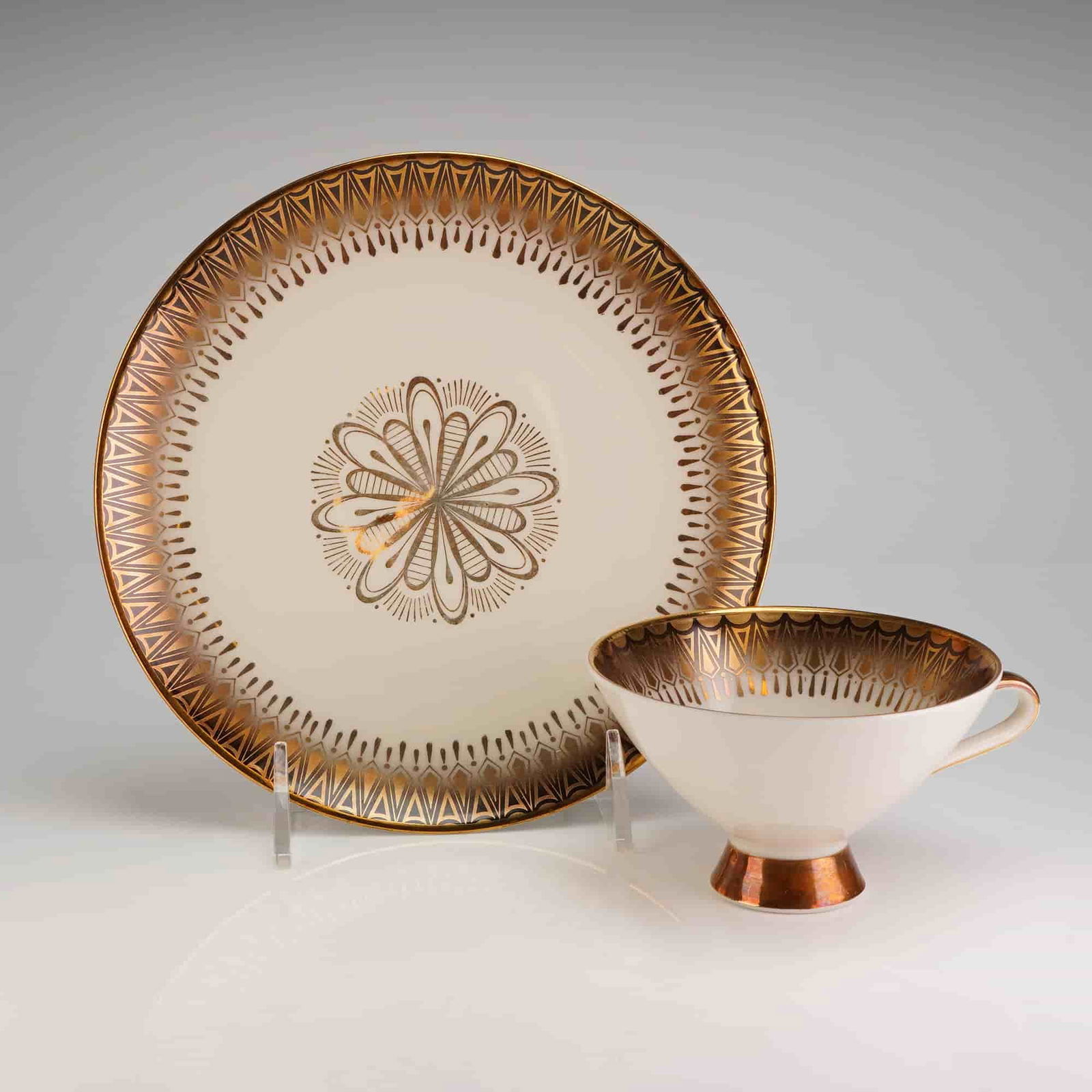 Winterling Marktleuthen Bavaria Gilt Porcelain Tea Cup and Saucer: A two-piece porcelain place setting consisting of one cup and one circular plate, manufactured by Winterling Marktleuthen, Bavaria. The set is executed in a Mid-Century Modern style featuring a cream-