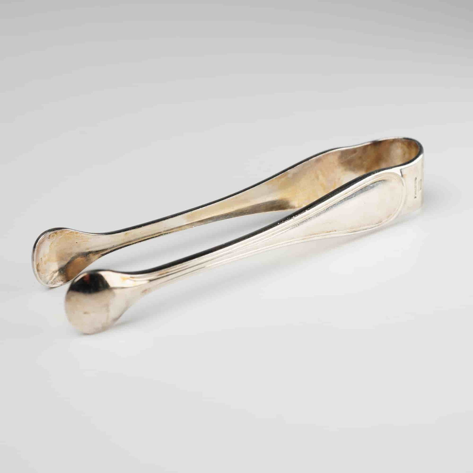 Christofle Silver Plate Sugar Tongs: A Christofle silver plate sugar tongs, characterized by a classic, understated design with gently curved arms and rounded, spoon-like grips. The item bears the prominent 'CHRISTOFLE' name, a square ha