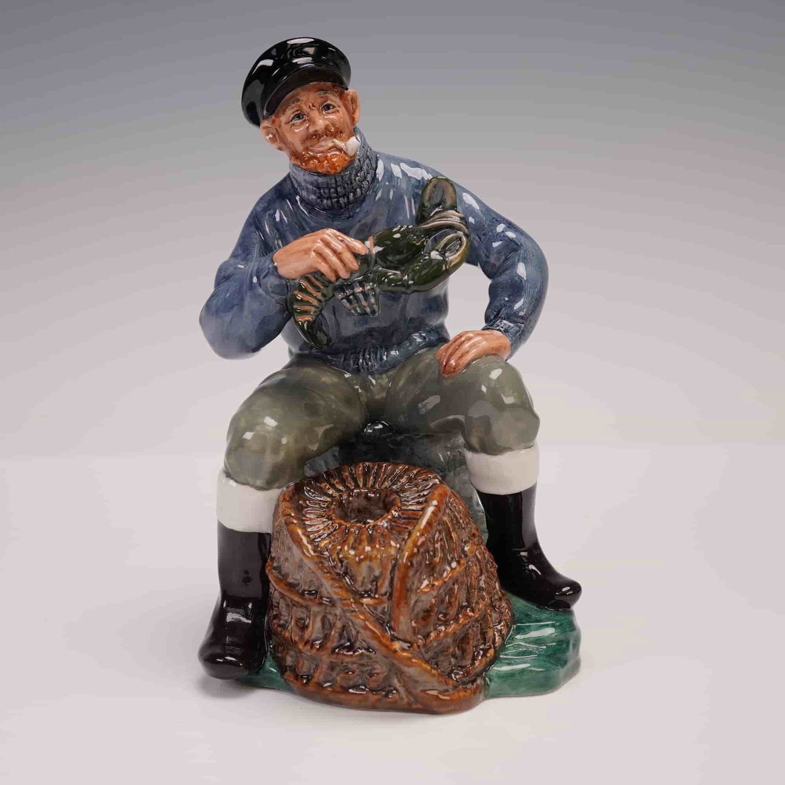 Royal Doulton Figurine, The Lobster Man HN2317: Hand-painted Royal Doulton bone china figurine depicting an old fisherman seated beside a wicker creel and holding a lobster. Designed by Mary Nicoll in glossy enamels with fine facial detail and mari