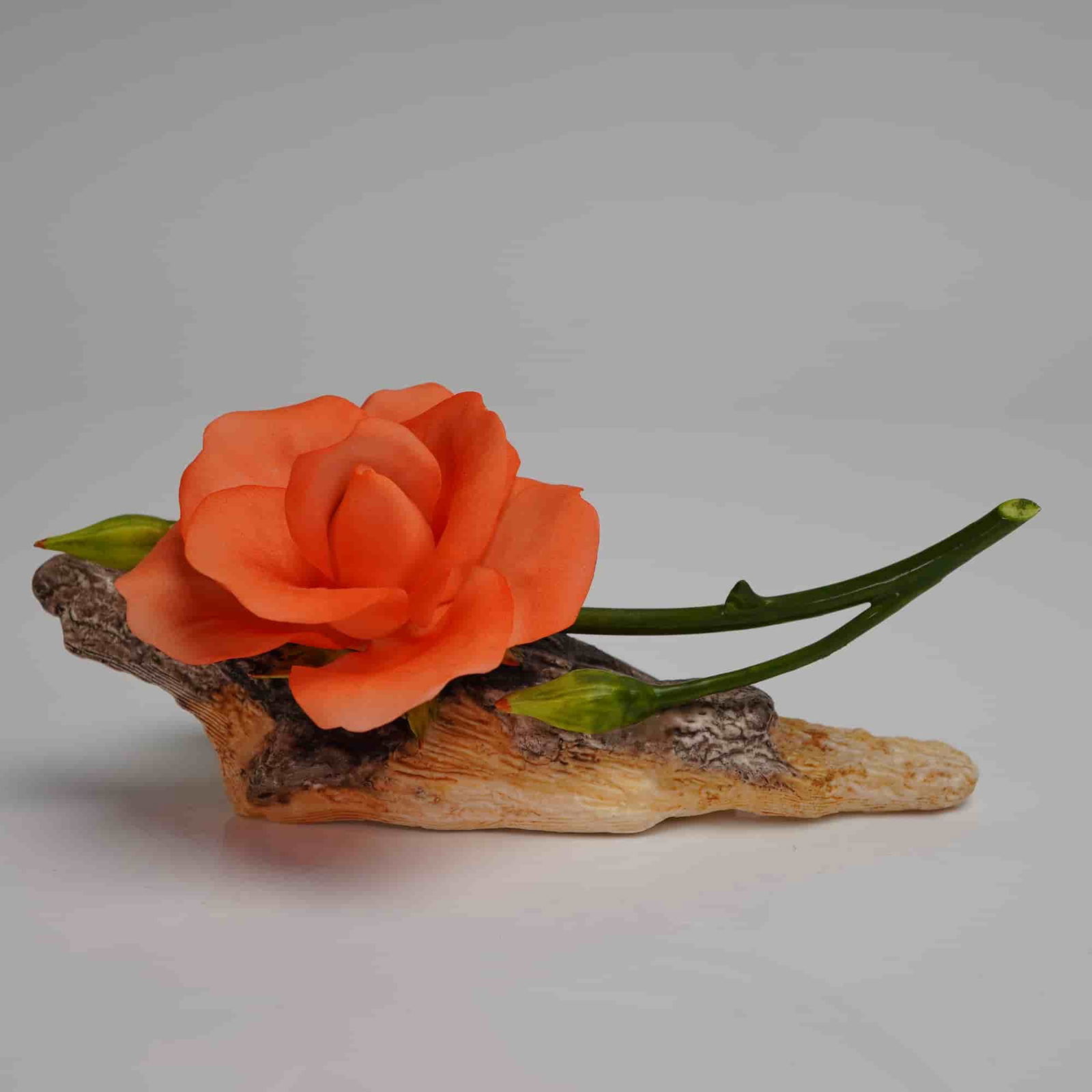 Boehm Bone Porcelain Coral Rose Sculpture 200-55-S: A single naturalistic floral sculpture crafted from Boehm Bone Porcelain, model number 200-55-S. The piece depicts an open rose in vibrant coral/orange hues, accompanied by a thorny green stem and