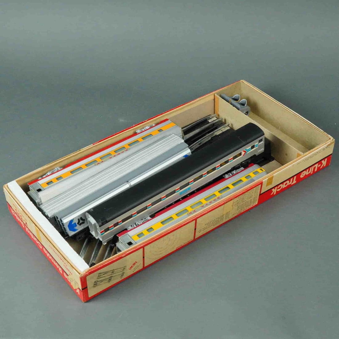 K-Line O Gauge Passenger Train Car Collection with Remote Switch and Track: A collection of eight O Gauge model train components by K-Line, including four passenger cars and four track/switch accessories, presented in the original K-Line Track cardboard box. The passenger