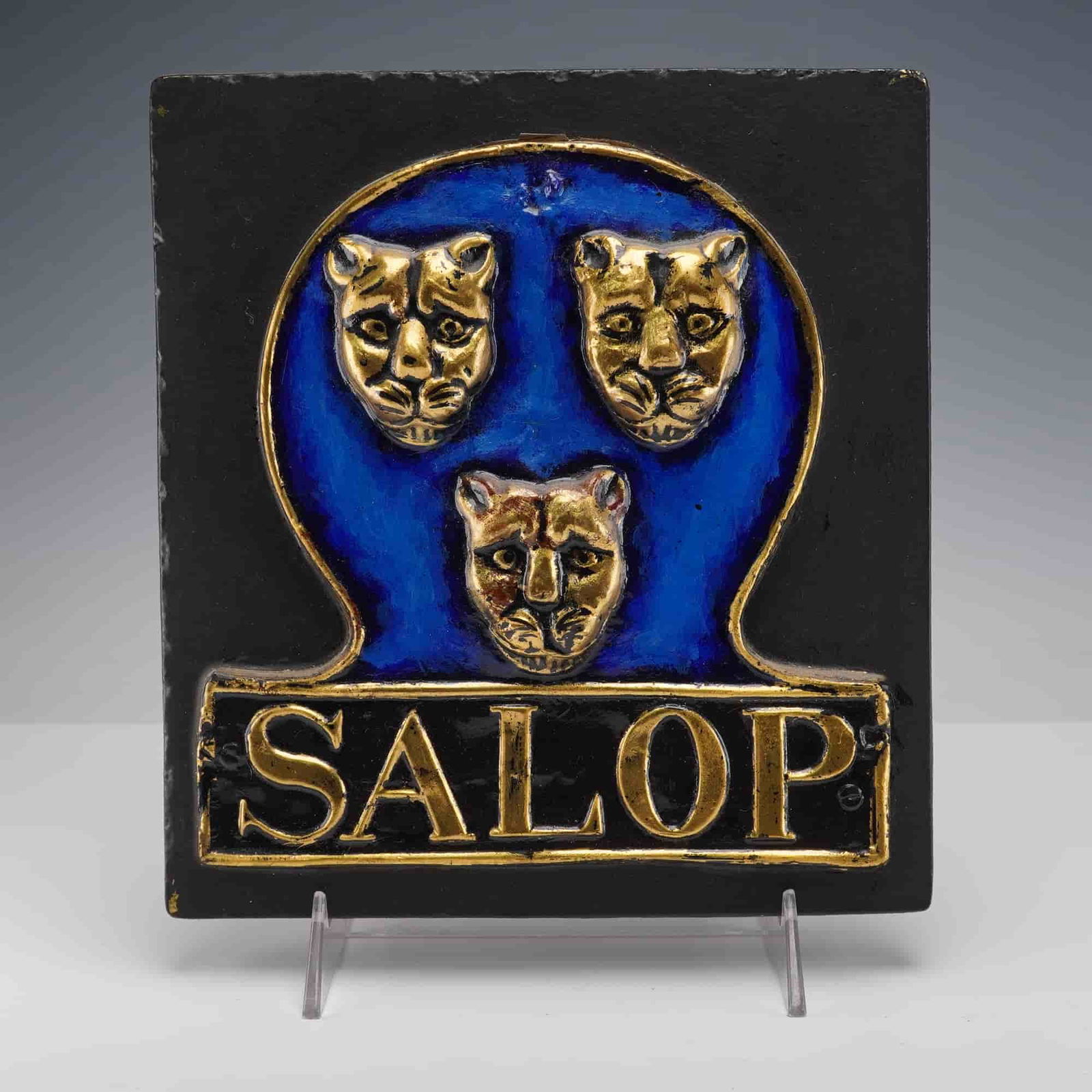Salop Insurance by E. V. Jackson Reproduction Fire Mark Plaque: This plaque shows three raised gold leopard heads on a deep blue shield above a gold Salop banner. It is mounted on a black backing and has a label on the reverse noting it is a reproduction of an ori