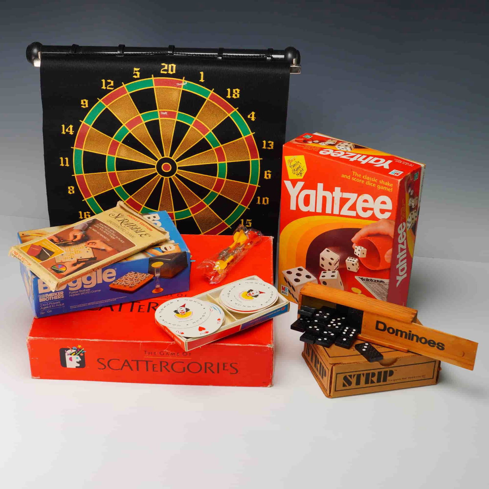 8pc Vintage Board & Parlor Games, Including Yahtzee and Scrabble: A nostalgic 8-piece lot of vintage family and parlor games, including Yahtzee, Scattergories, Boggle, and a pocket edition of Scrabble. Also included are a soft dartboard, a wooden domino set, round p