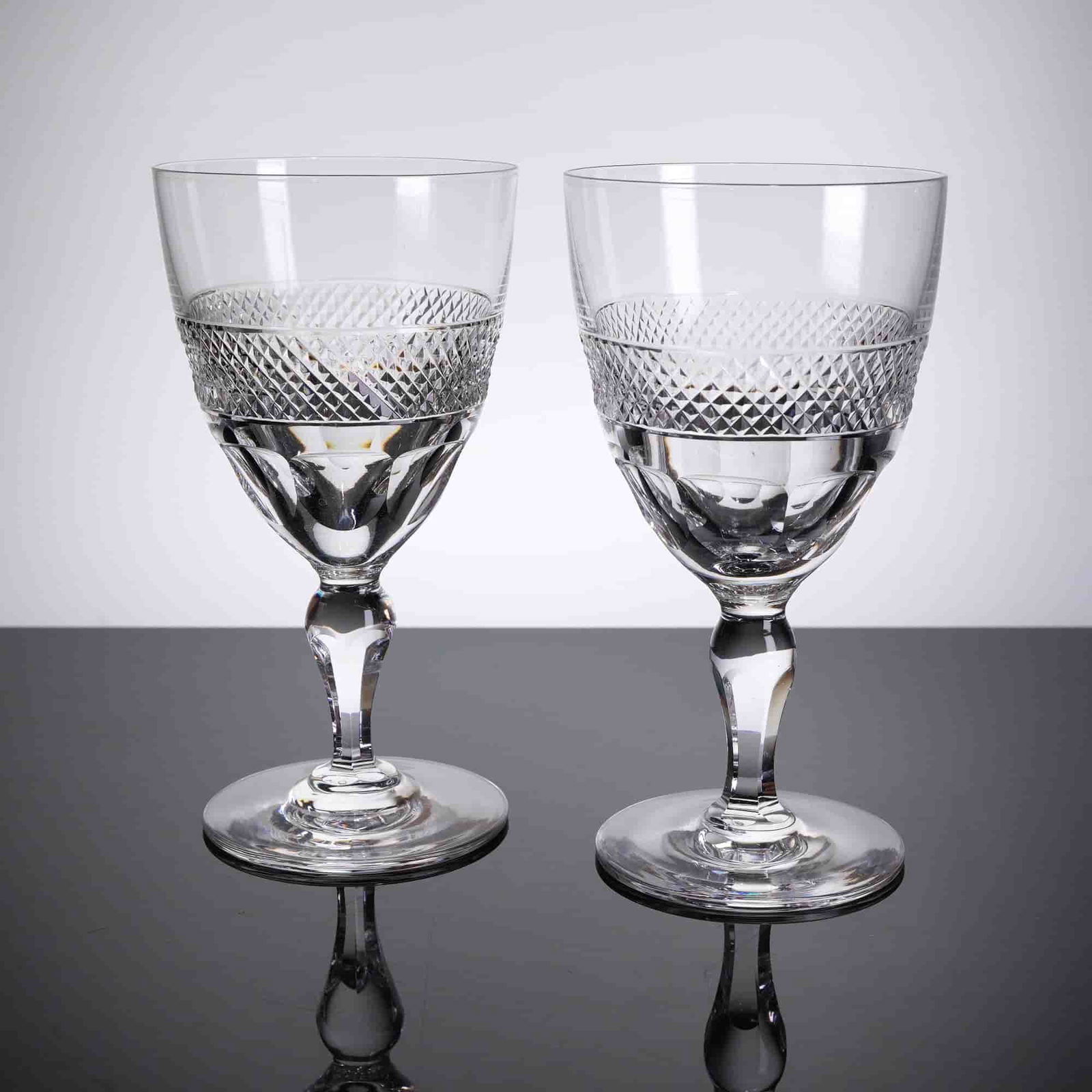 A Pair of Orrefors Sherry Glasses, Rio Patern: A pair of cut crystal stemmed glasses from Orrefors in the Rio patern. Each glass features a clear, smooth upper bowl section transitioning to a dense band of diamond and cross-hatch cutting around th