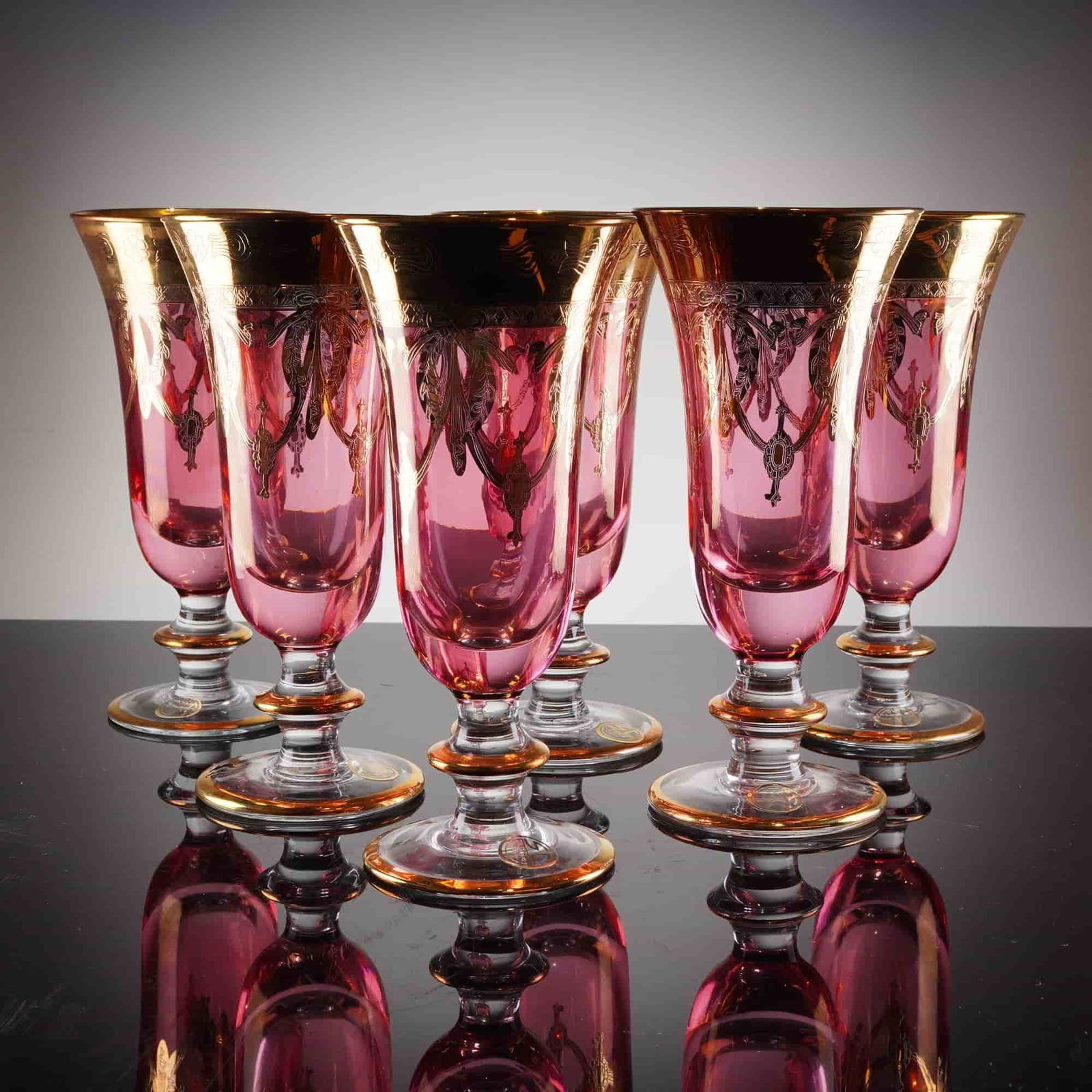 6pc SC Line Italian Cranberry Pink Iced Tea Glasses: A collection of six stemmed glasses manufactured by SC Line, featuring a tall, fluted bowl constructed of cranberry pink glass supported by a clear, stepped stem and circular foot. The glasses are
