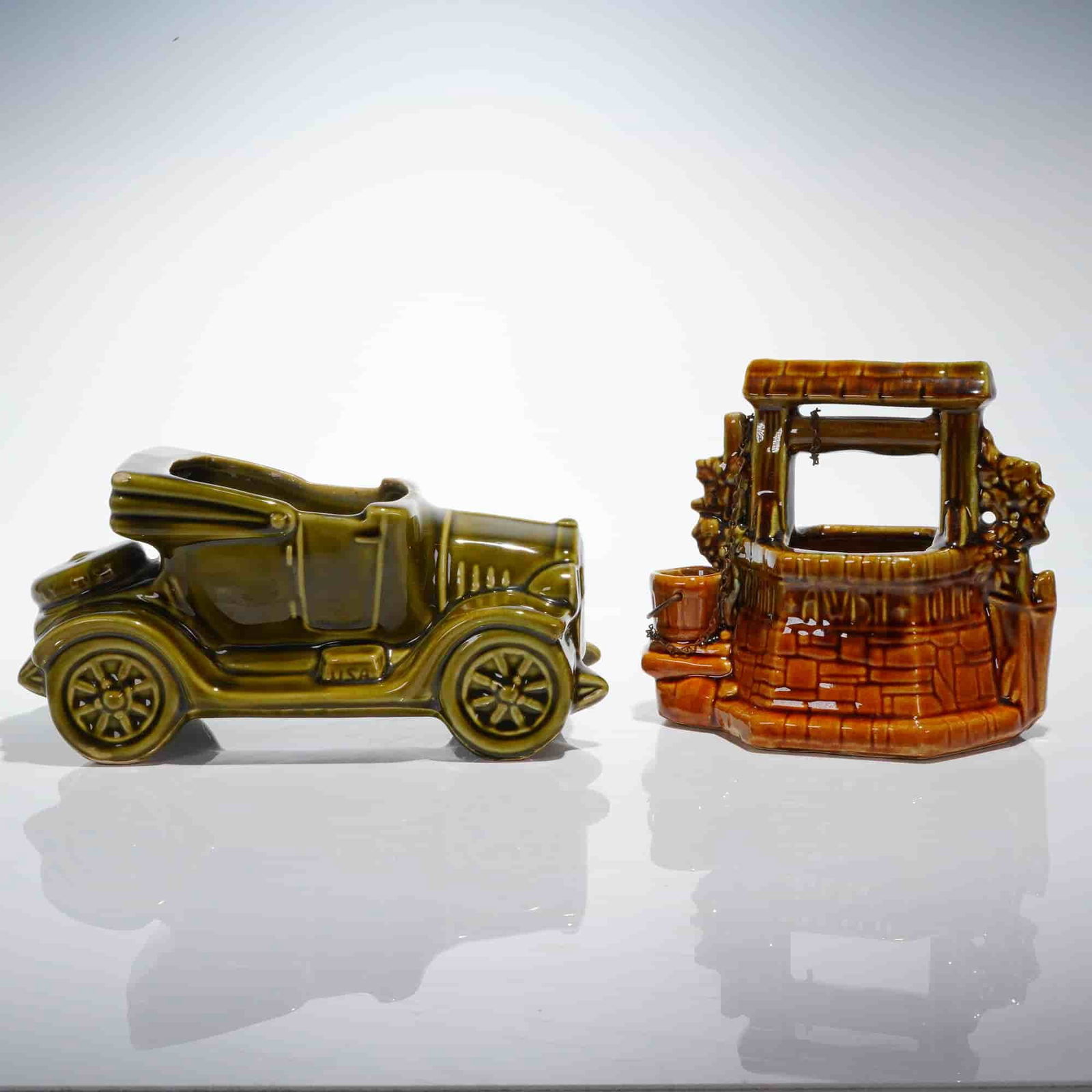A Pair of McCoy Pottery Decorative Car and Wishing Well Planters: This lot presents a 2pc collection of vintage decorative glazed ceramic containers manufactured by McCoy Pottery, USA. The first piece is an antique automobile-shaped planter, commonly identified as