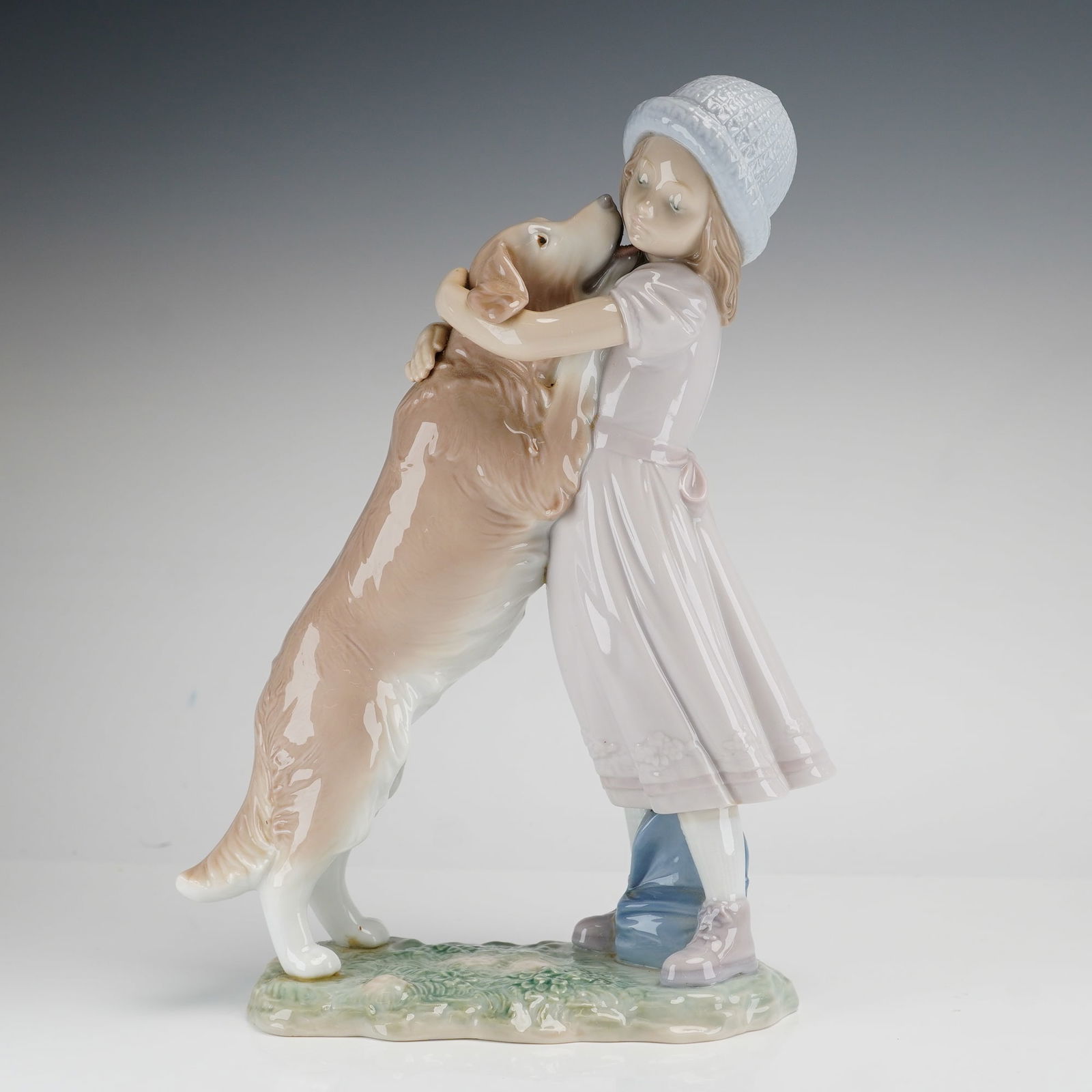 Lladro A Warm Welcome Porcelain Figurine Model 6903: A fine glazed porcelain figurine produced by Lladro, titled A Warm Welcome (Mi Bienvenida), model number 6903. The piece depicts a young girl wearing a textured white knit hat and a pale pink dress as