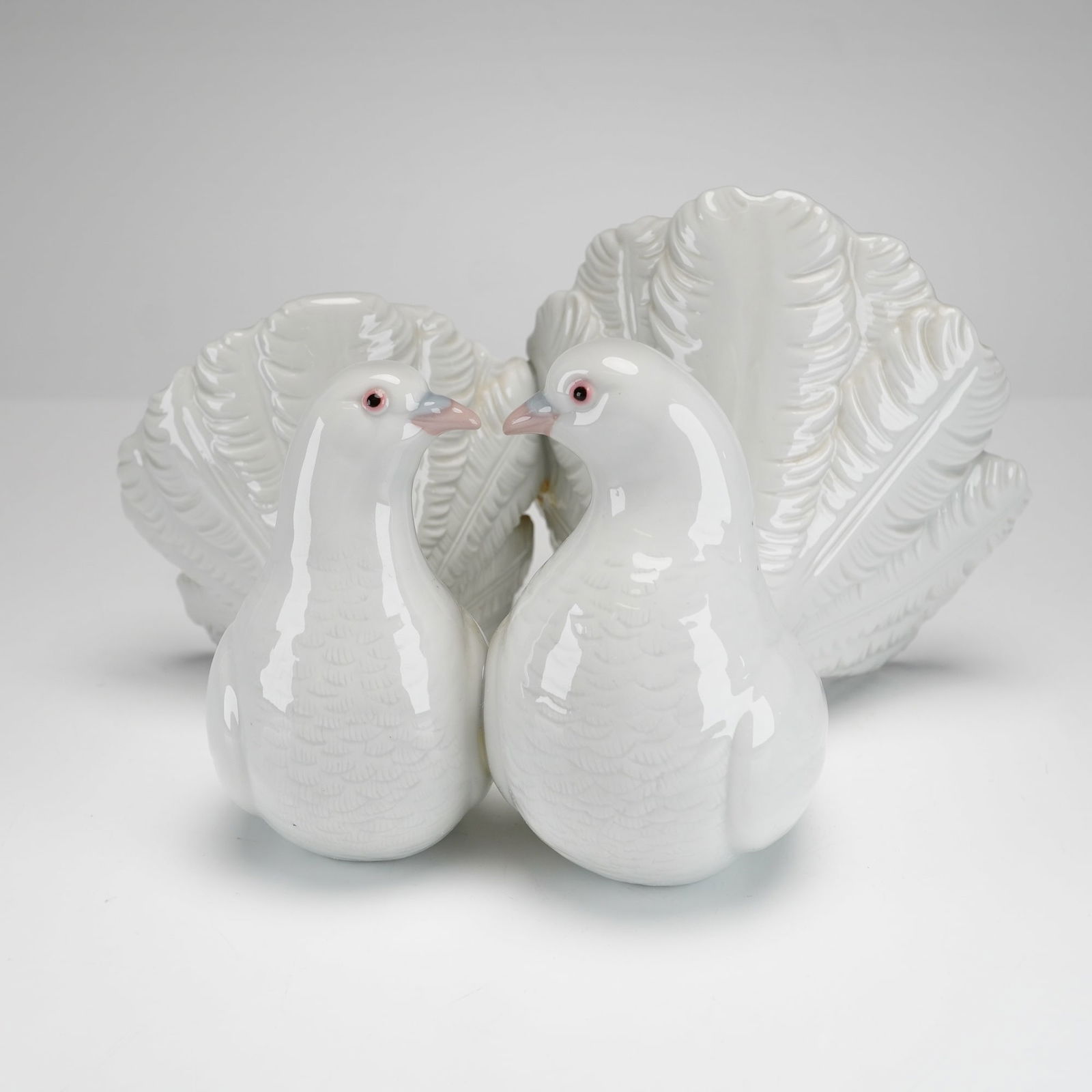 Lladro Porcelain Figurine, Couple of Doves 1001169: A glazed porcelain figurine depicting a pair of doves in a courtship pose. The piece is finished in a pure white gloss with delicate pink highlights on the eyes and beaks. The base features the blue L