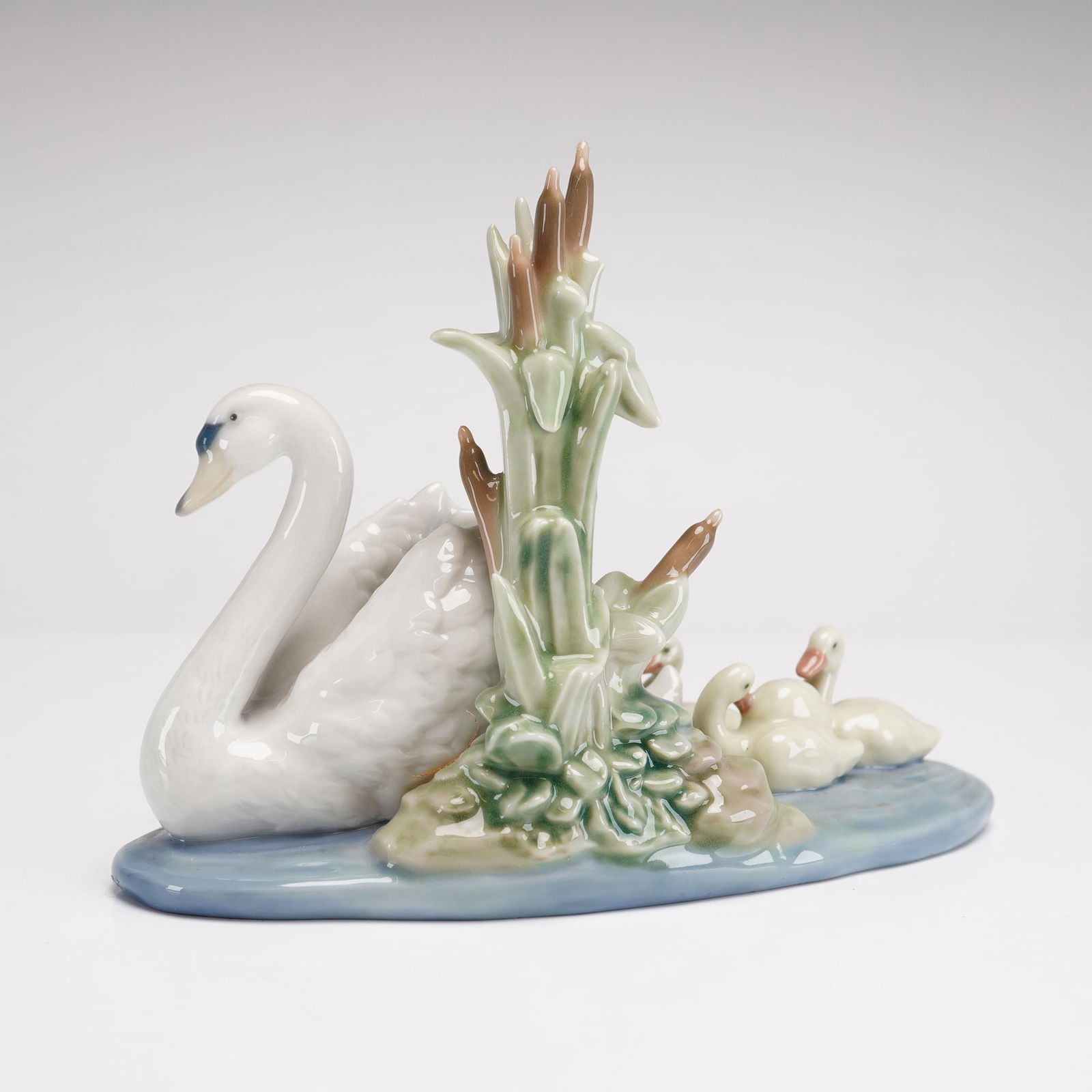 Lladro Porcelain Figurine, Follow Me 1005722: This Lladro glazed porcelain figurine, model number 5722, is titled Follow Me. The subject features a large mother swan swimming on a pale blue water-textured base accompanied by four cygnets. The com