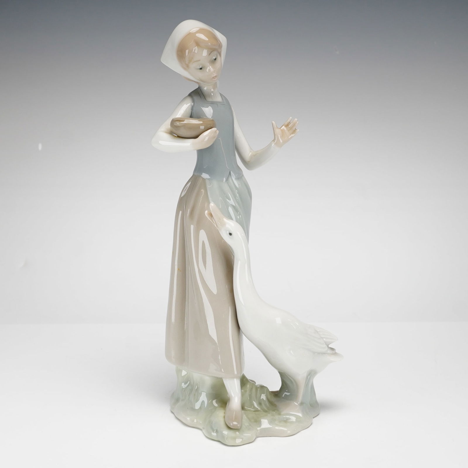 Lladro Porcelain Figurine, Girl with Duck 1001052: This is a classic Lladro porcelain figurine titled Girl with Duck, model number 1052. The piece depicts a young girl in traditional peasant attire, including a long skirt, apron, and headscarf. She is