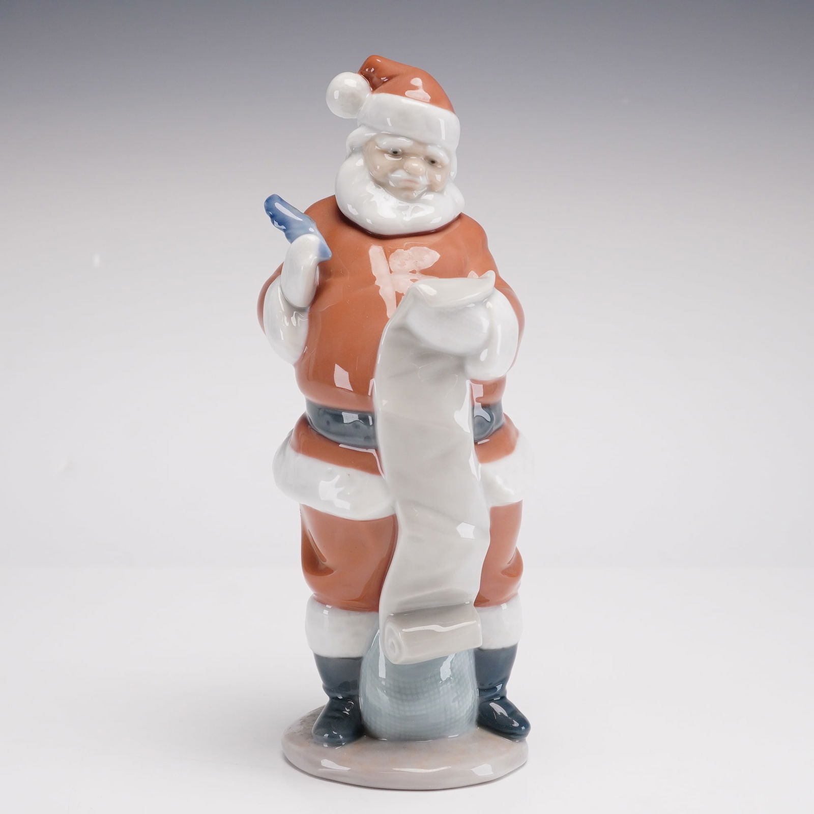Lladro Porcelain Figurine, Santa's List 1006657: This glazed porcelain figurine by Lladro, titled Santa's List (model number 1006657), depicts Santa Claus in his traditional red suit with white fur-like trim, black boots, and a grey belt. He is show