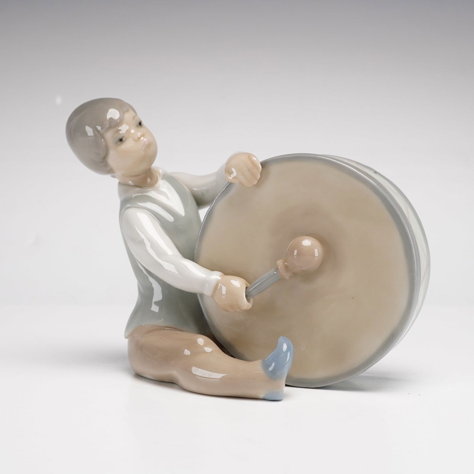 Lladro Porcelain Figurine, Boy Playing Drum 1004616: This is a vintage Lladro glazed porcelain figurine titled Boy Playing Drum, model number 4616. The piece depicts a young boy seated on the ground, leaning forward to play a large bass drum. He is dres