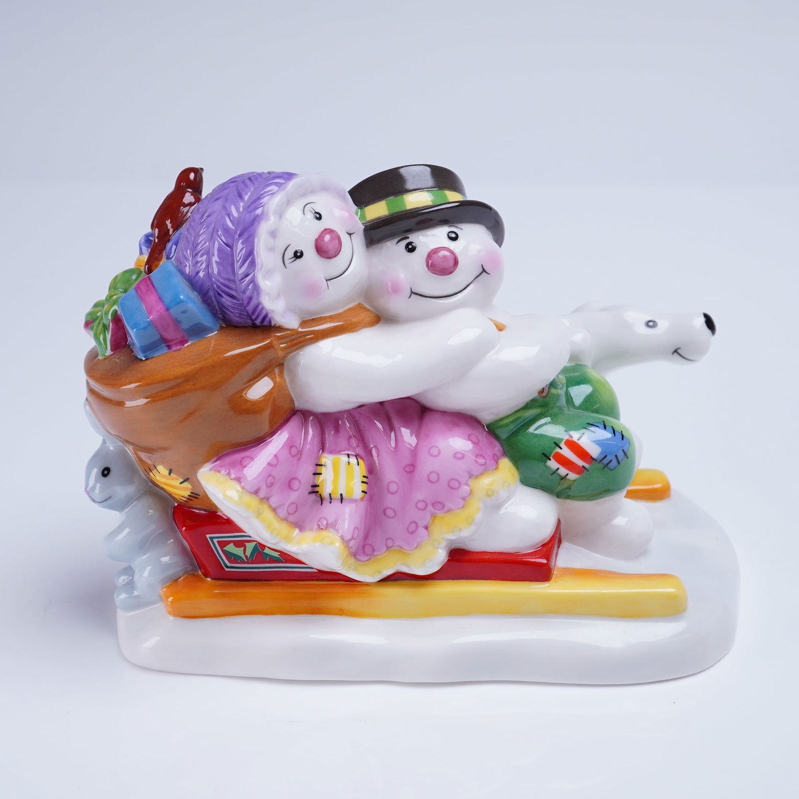 Royal Doulton Figurine, Frosty Family Collection, Snowdrift Leads The Way: A hand-made and hand-decorated bone china figurine by Royal Doulton, titled Snowdrift Leads The Way, from the Frosty Family collection. The piece depicts two embracing snowmen, one wearing a purple kn
