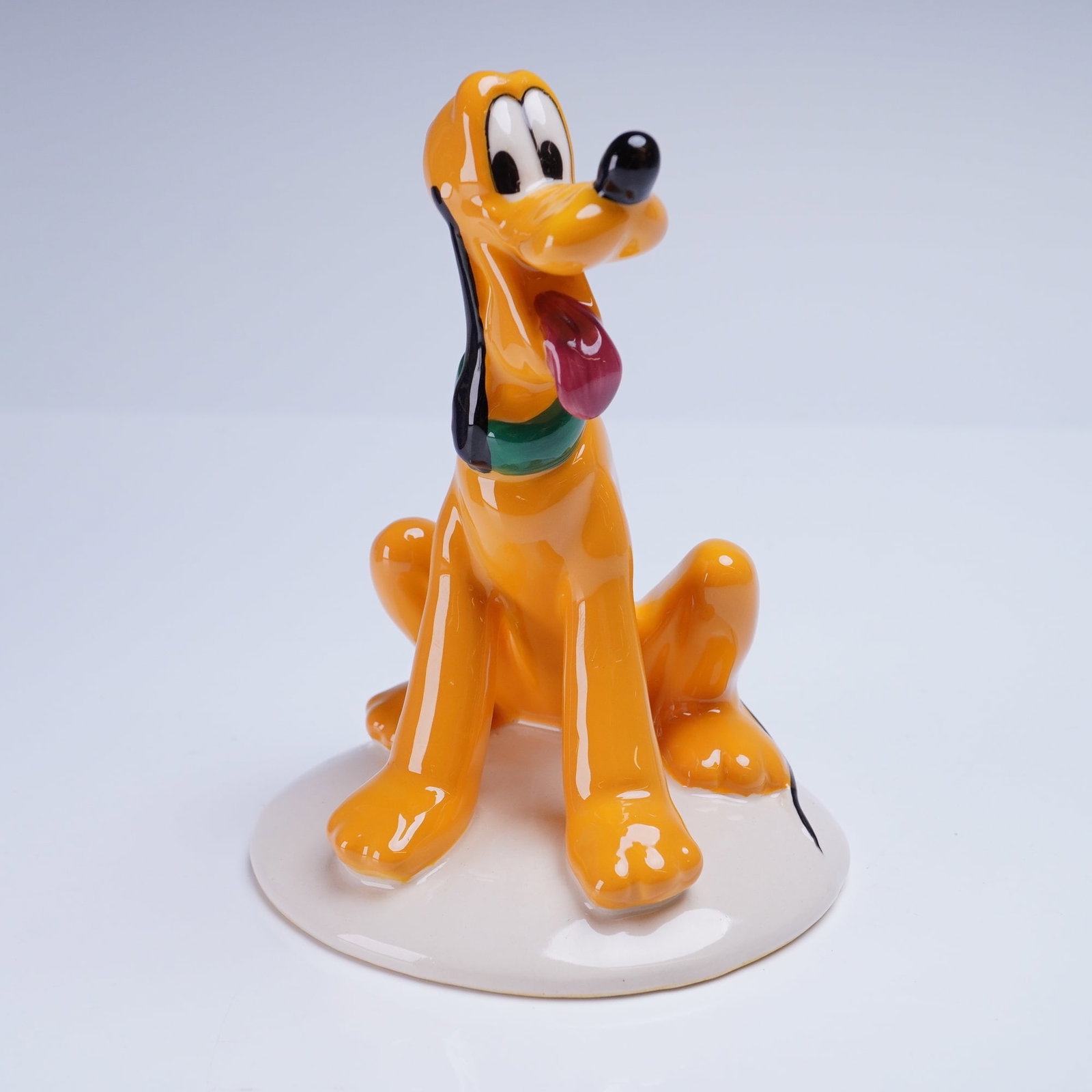Royal Doulton The Mickey Mouse Collection Figurine, Pluto 70th Anniversary: A glazed ceramic figurine depicting the Disney character Pluto, part of The Mickey Mouse Collection produced by Royal Doulton. The figurine is rendered in glossy orange, black, green, and red enamels,
