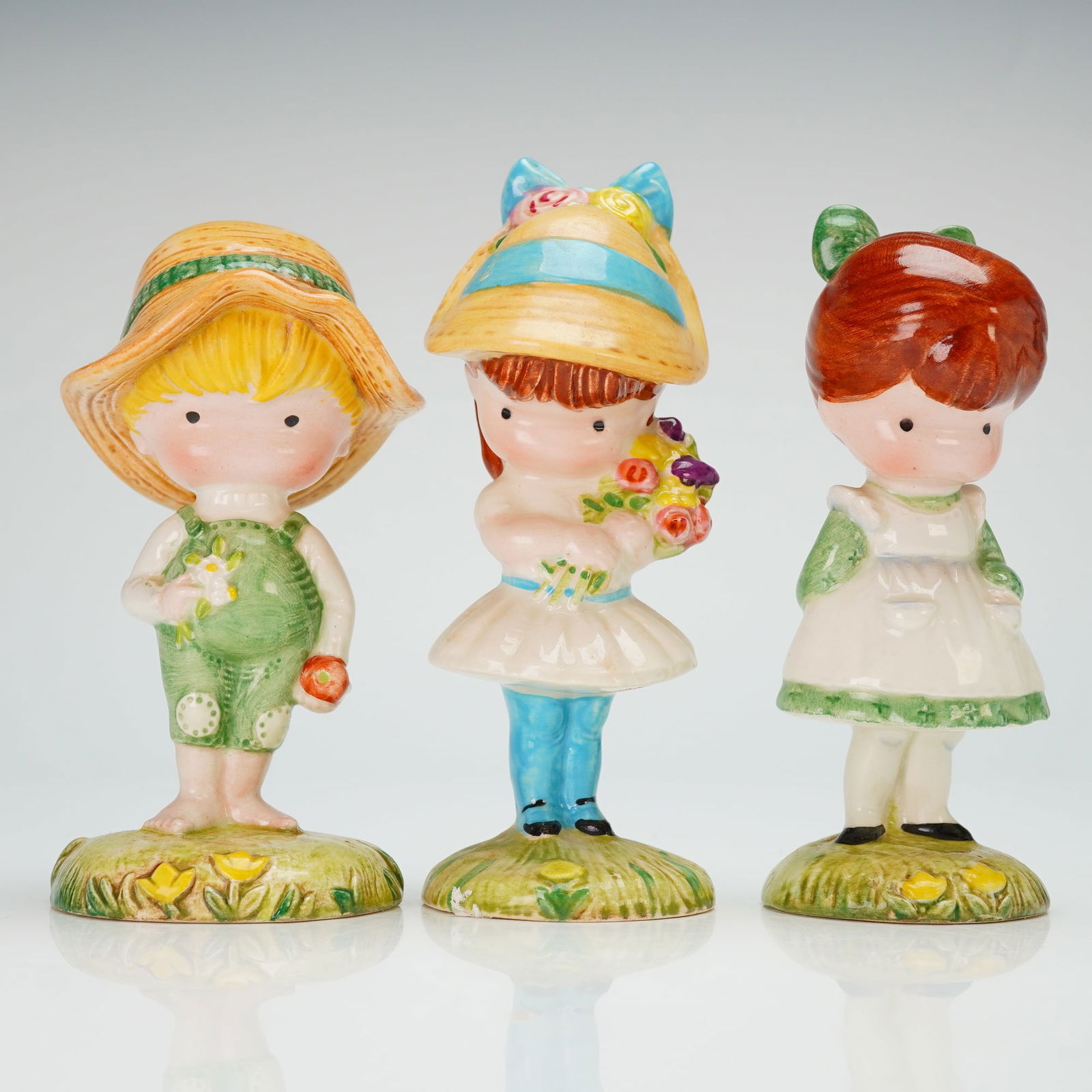 3pc Beswick Joan Walsh Anglund Ceramic Figurines: A trio of glazed ceramic figurines manufactured by Beswick, England, based on the designs of Joan Walsh Anglund. The collection includes three distinct figures: a boy wearing a wide-brimmed straw hat