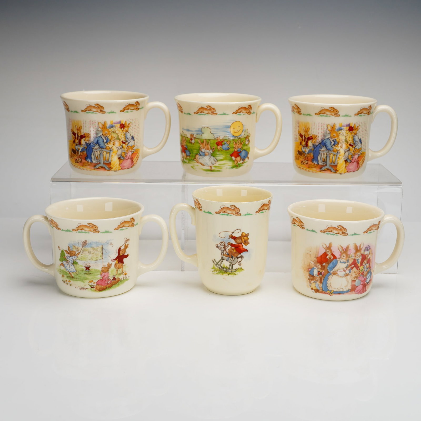 6pc Royal Doulton Bunnykins Bone China Mugs & Two-Handled Cup: A collection of six Royal Doulton Bunnykins fine bone china child's mugs and a two-handled cup, also known as a hug-a-mug. The items feature classic transfer-printed illustrations of anthropomorphic r
