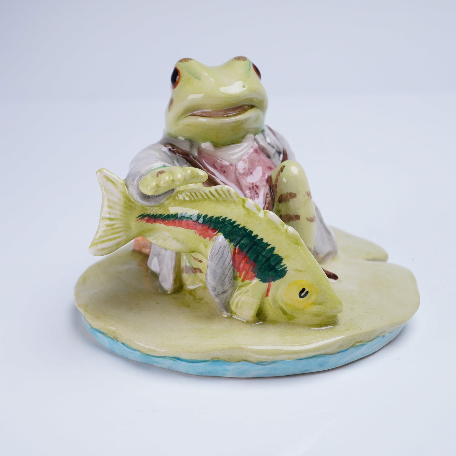 Beswick Beatrix Potter Figurine, Jeremy Fisher Catches a Fish: A glazed ceramic figurine from the Beswick Beatrix Potter series, titled "Jeremy Fisher Catches a Fish." The piece depicts the anthropomorphic frog character, Jeremy Fisher, seated on a lily pad base