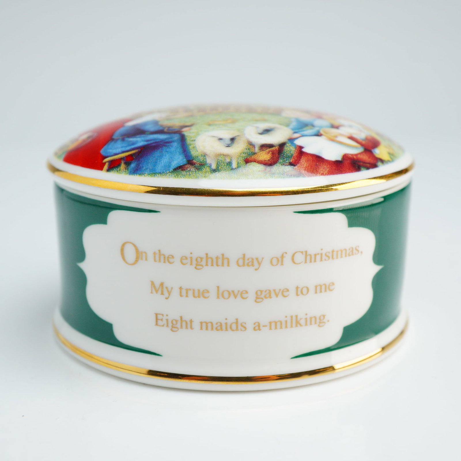 Wedgwood Bone China Lidded Box, Eight Maids a-Milking: This Wedgwood round bone china lidded box is part of the Twelve Days of Christmas series, specifically commemorating the eighth day. The cylindrical vessel features a dark green exterior wall accented