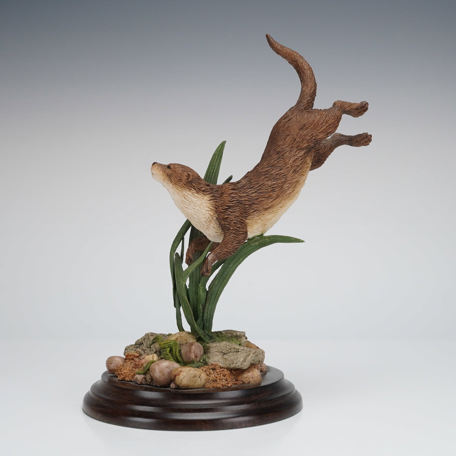 Country Artists Otter Swimming Figurine: A wildlife figurine crafted by Country Artists of Stratford-upon-Avon, England. The naturalistic sculpture depicts a brown otter swimming, supported by tall green reeds and foliage rising from a simul