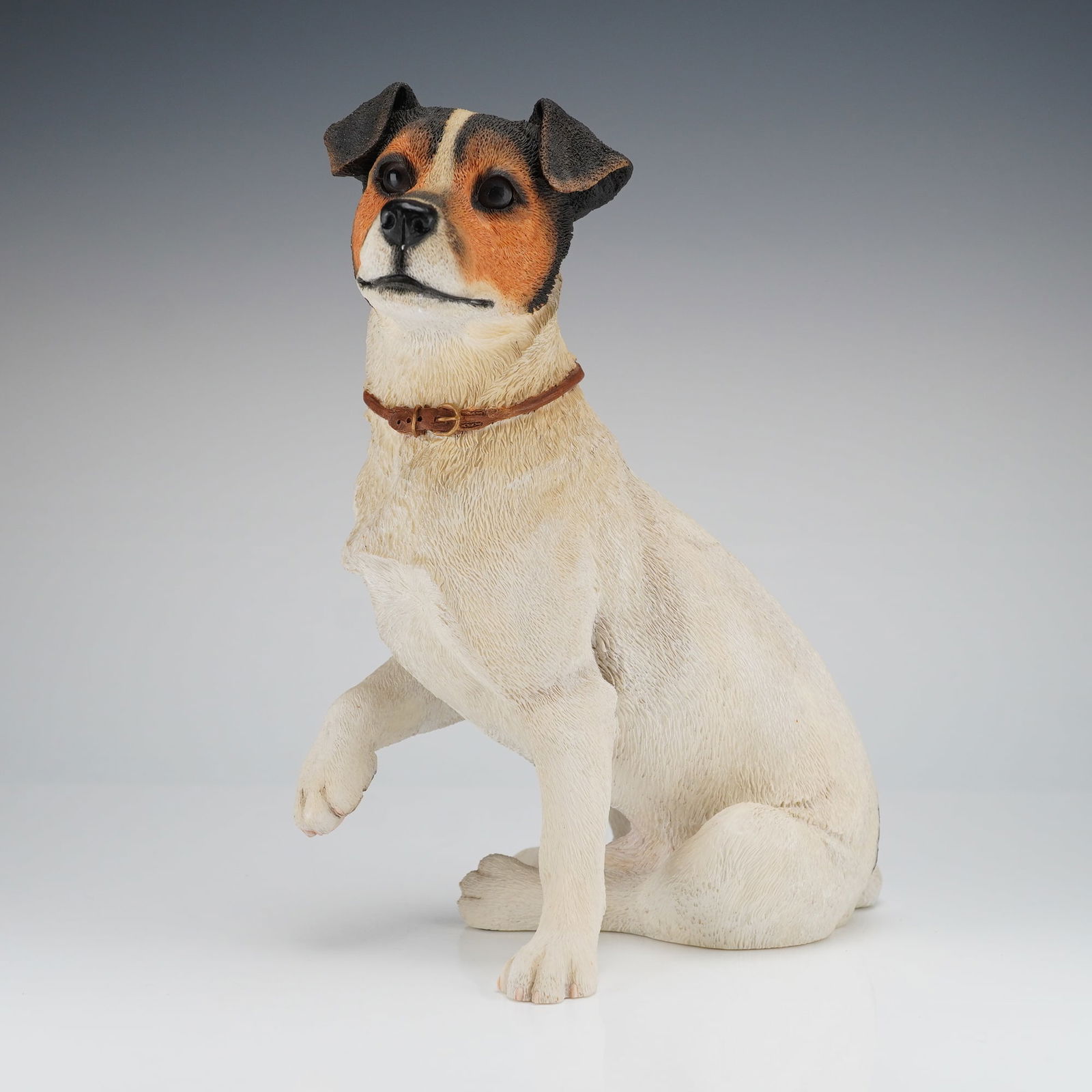 Country Artists Top Dogs Sculpture, Jack Russell: The sculpture, crafted from resin or composite material, depicts the dog in a seated pose with its right front paw raised. The coloration is realistic, featuring white body fur with black, tan, and or