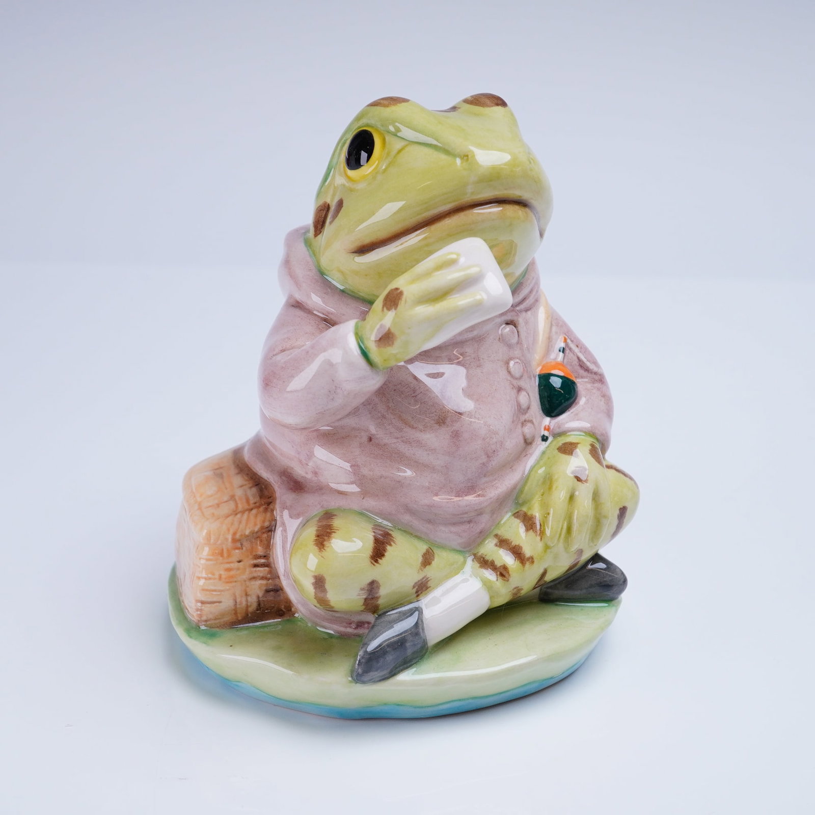 Royal Albert Beatrix Potter Figurine, Jeremy Fisher: A glazed figurine manufactured by Royal Albert, depicting the anthropomorphic character Jeremy Fisher from the Beatrix Potter stories. The figure is modeled as a frog seated on a pale green and blue l