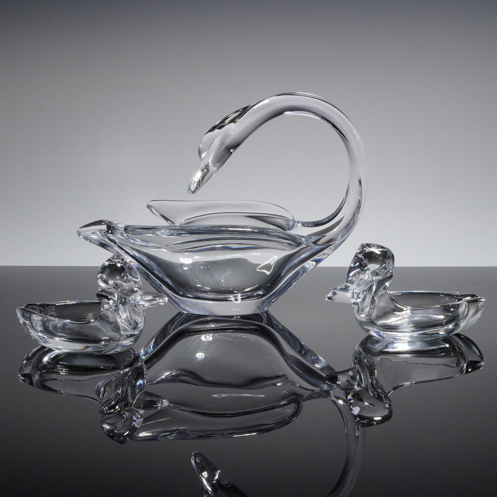 A Three-Piece Vannes-le-Chatel Crystal Swan Dish and Duck Ashtrays Set: A three-piece set of clear, colorless heavy crystal decorative tableware attributed to Vannes-le-Chatel, France. The collection comprises one large centerpiece bowl stylized as a swan with an elegantl