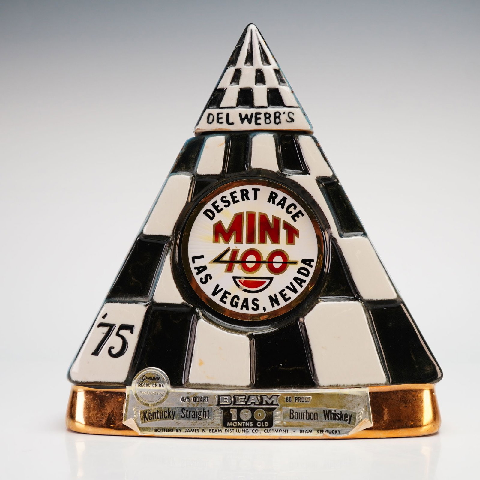 Jim Beam Regal China Del Webb's Mint 400 Desert Race Commemorative Whiskey Decanter, 1975: This vintage 1975 commemorative whiskey decanter was manufactured by the Regal China Corporation for the James B. Beam Distilling Co. Designed by C. Miller, the ceramic vessel features a distinctive