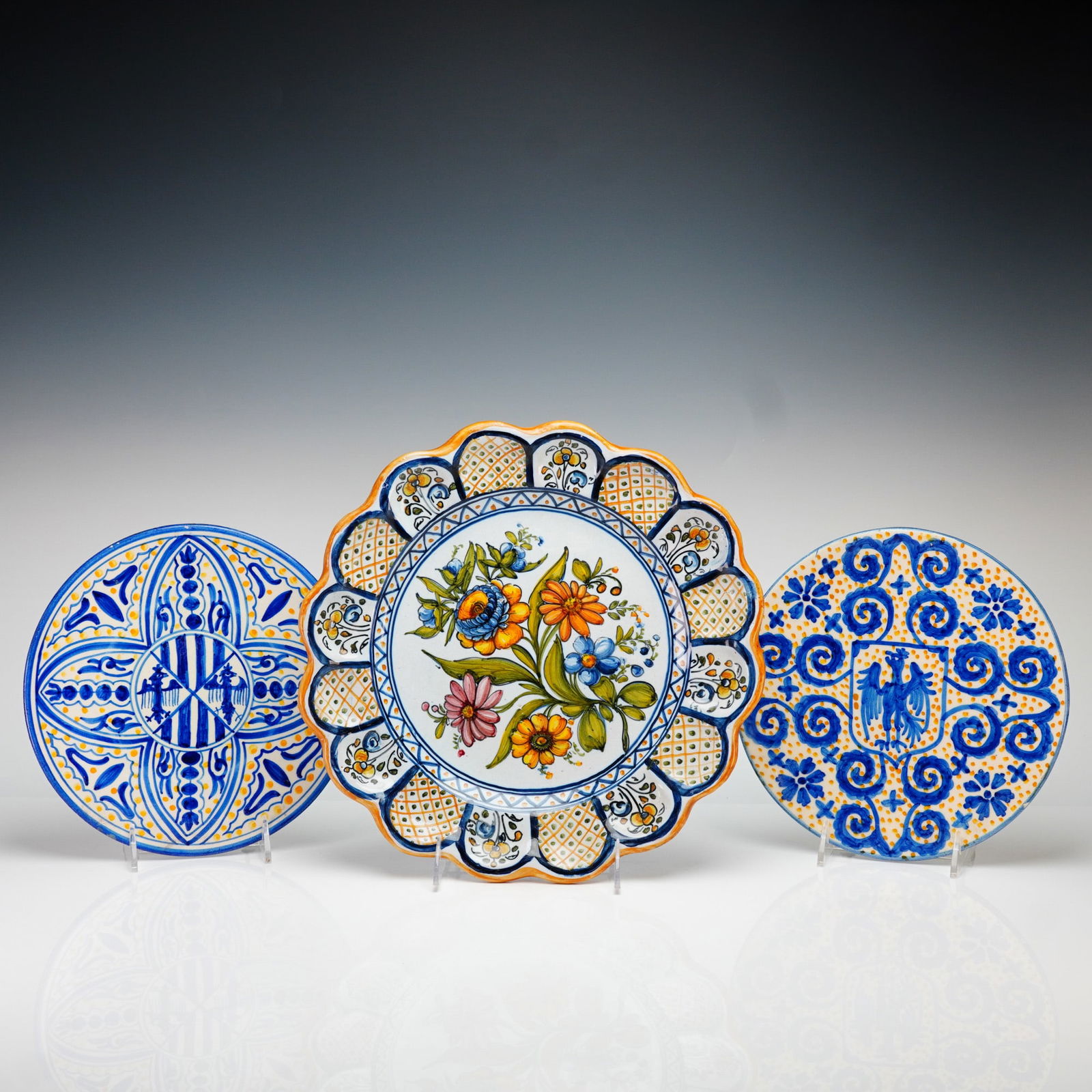 Talavera de la Reina Spanish Hand-Painted Floral and Heraldic Wall Plates: This collection features three hand-painted pottery wall plates from Spain, executed in traditional tin-glazed earthenware. The largest plate is designed with a deep-scalloped molded rim and a central